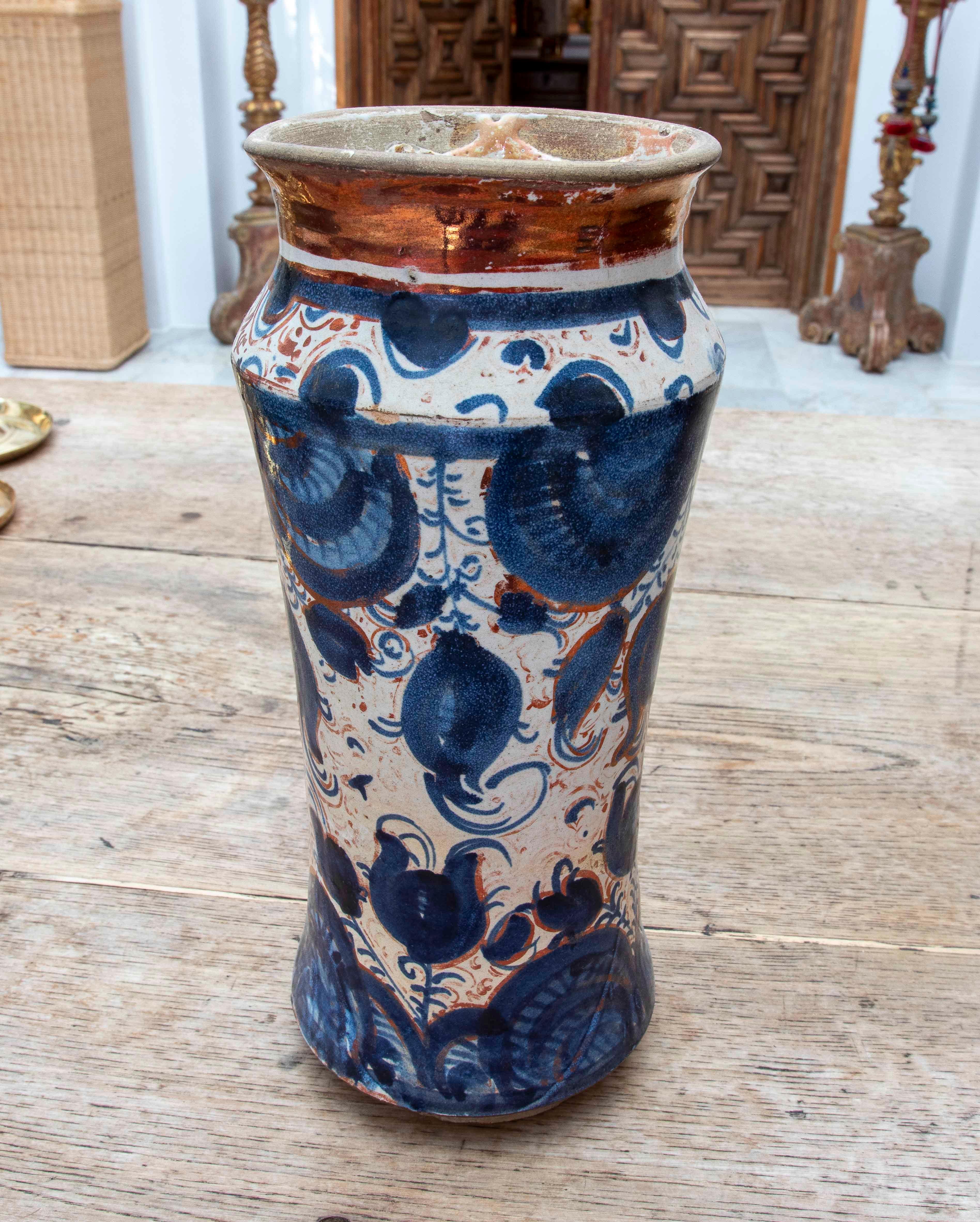 Magnífico jarrón o albarelo de cerámica de Talavera, decorado a mano con motivos vegetales estilizados en azul cobalto y rojo óxido sobre fondo blanco marfil, rematado con un característico vidriado cobrizo, típico de las técnicas hispanomusulmanas