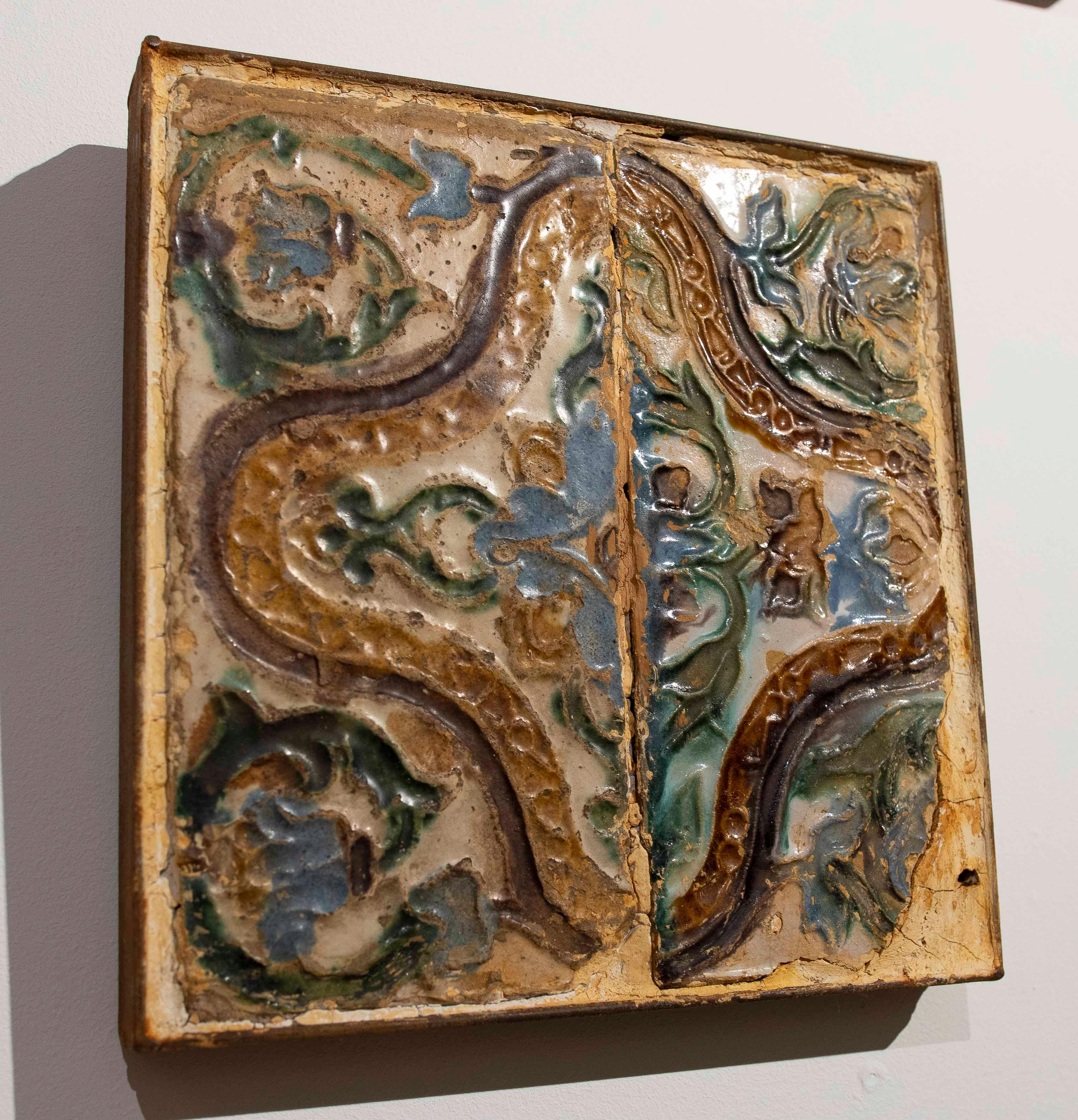 Pair of antique 16th-century tiles, made using the cuerda seca technique and framed in iron.
These framed antique tiles are decorated with an organic relief design in shades of green, blue, brown, and cream. The surface exhibits crackling, wear, and