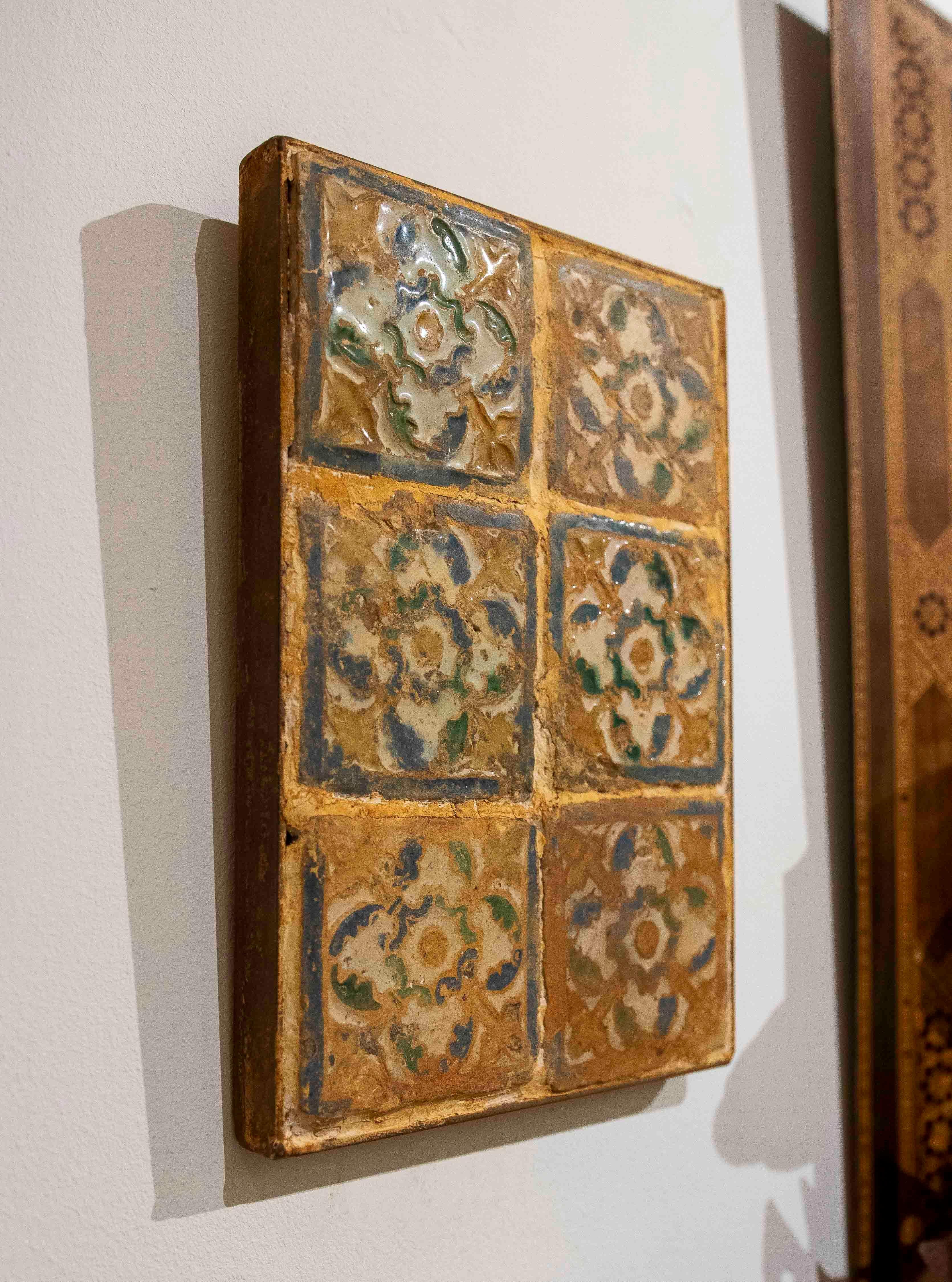 Antique 16th-century tile panel of six, made using the cuerda seca technique and framed in iron. The panel comprises six antique tiles decorated with floral motifs in shades of green, blue, and cream. The pieces show wear, crazing, and traces of