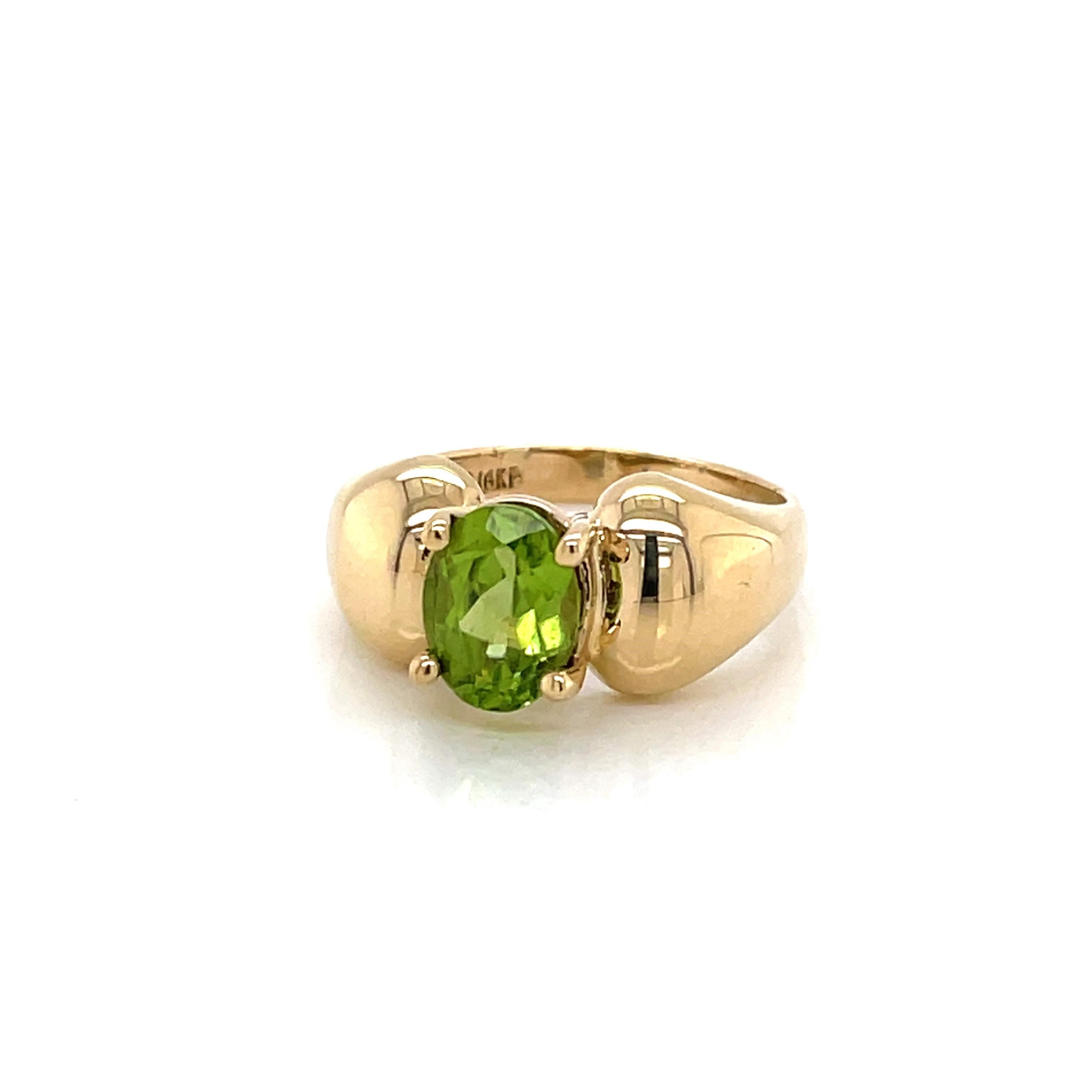 A vivid green 6x8mm oval faceted peridot stone is prominently featured and boldly framed by its uniquely contoured 10 karat yellow gold band. 
Peridot, a semi-precious tone, often thought to symbolize prosperity and good fortune, is also the