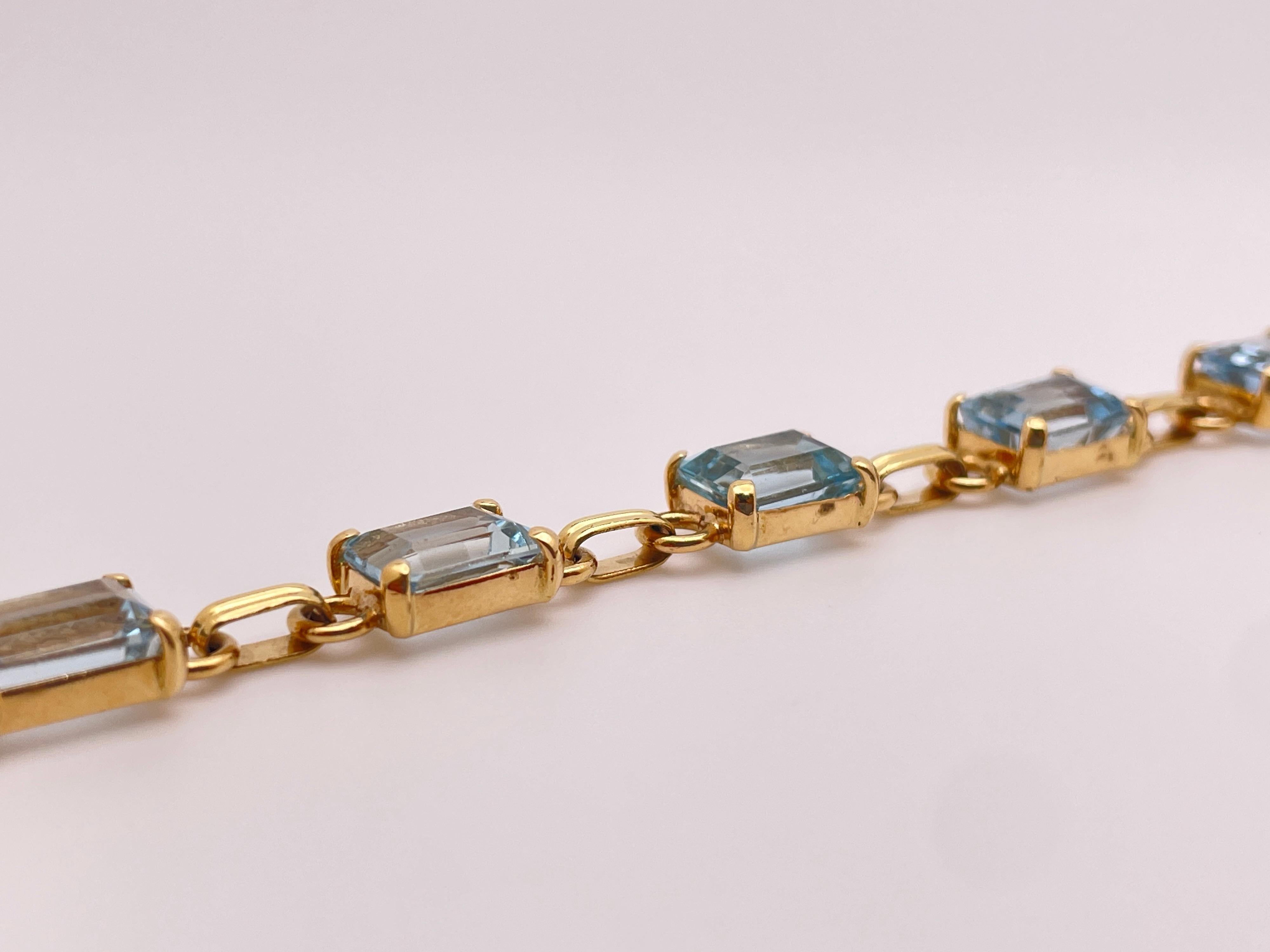 This elegant 14K yellow gold tennis bracelet showcases nine emerald-cut natural blue aquamarines, weighing a total of 16.56 carats (IGI Report #40J7955724). Each aquamarine measures 8.60 x 6.42 x 4.50 mm, displaying a beautiful, natural blue hue