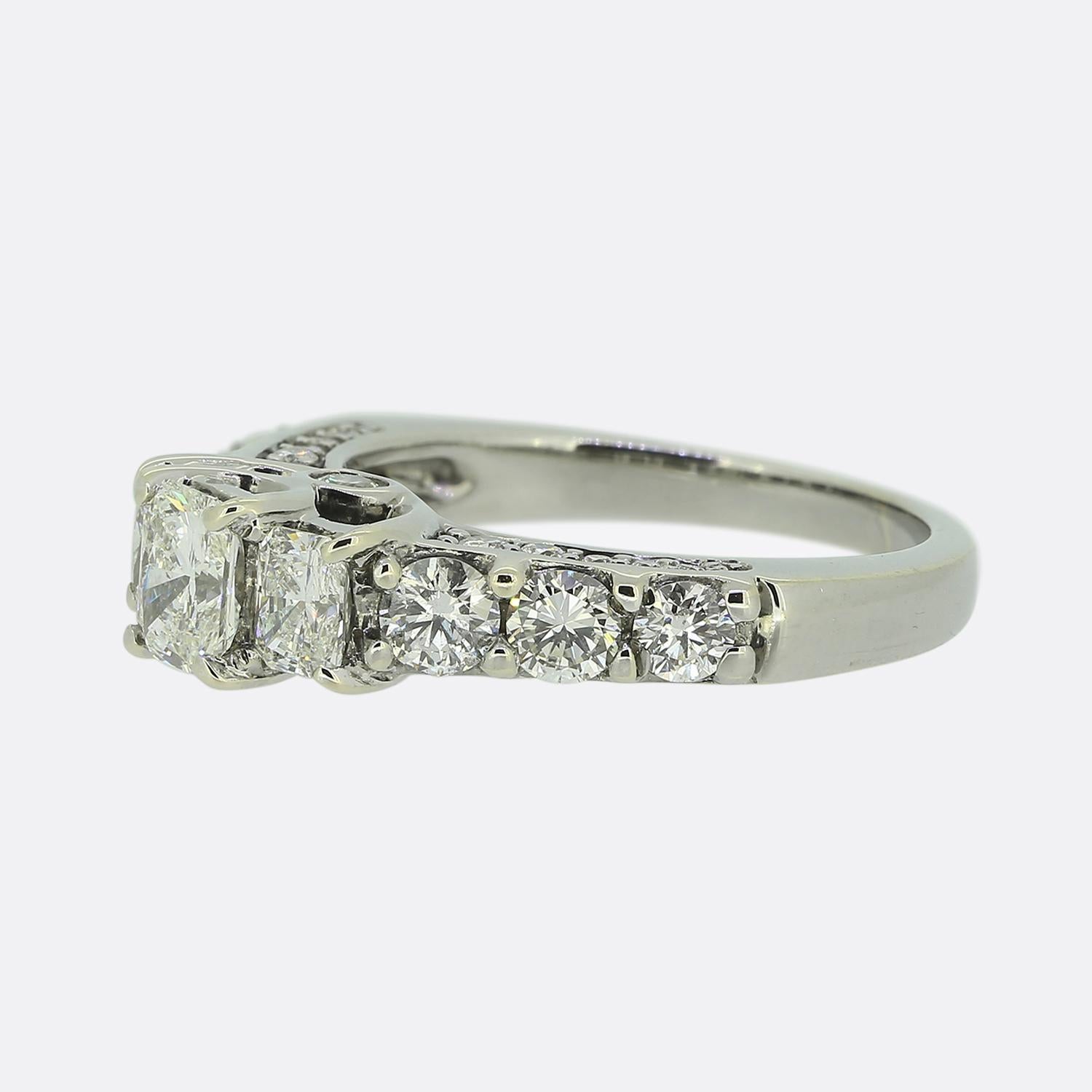 Ecco uno splendido anello con più diamanti. Questo pezzo unico è stato realizzato in platino e presenta un Trio di diamanti taglio radiante al centro del quadrante in una formazione a gradini. Queste pietre primarie sono poi affiancate su entrambe