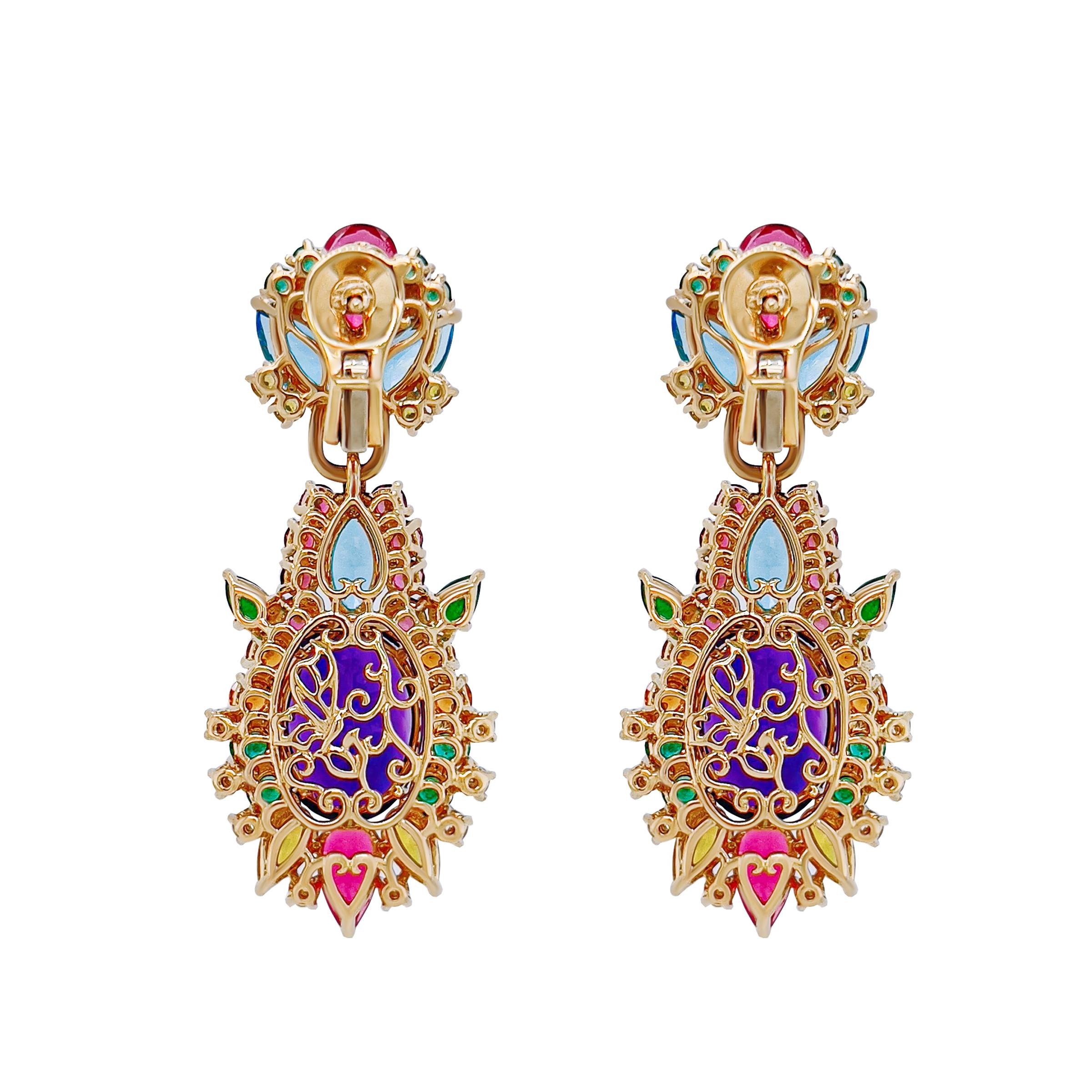 Set in 18k yellow gold, this pair of earrings showcase a lush abbundance of coloured gems. A natural amethyst centre stone totalling 117.04 carats is surrounded by an intricate selection of top quality natural coloured stones such as emeralds,