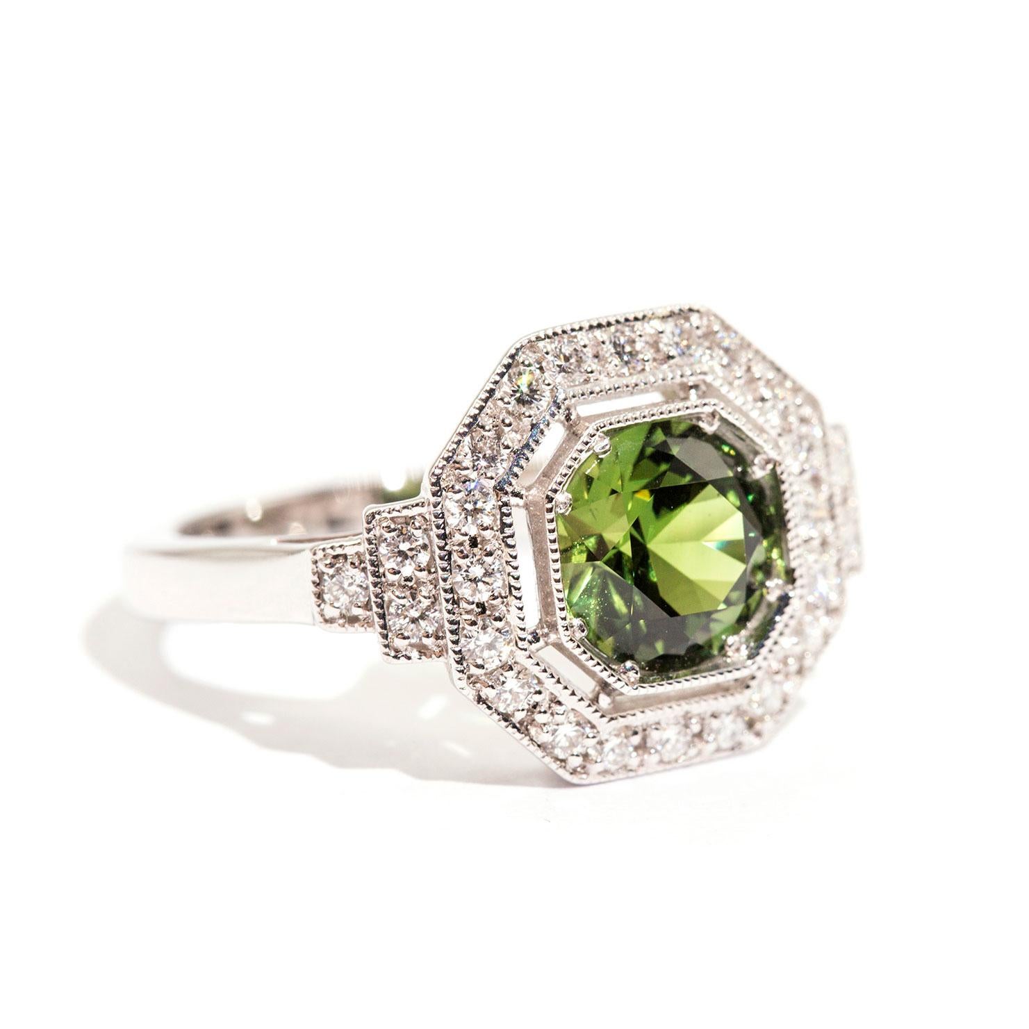 Forged in 18 carat white gold, this breathtaking art deco inspired ring features a captivating 1.71 carat bright green round natural sapphire with a gorgeous hexagonal border of shimmering round brilliant diamonds and six further round brilliant