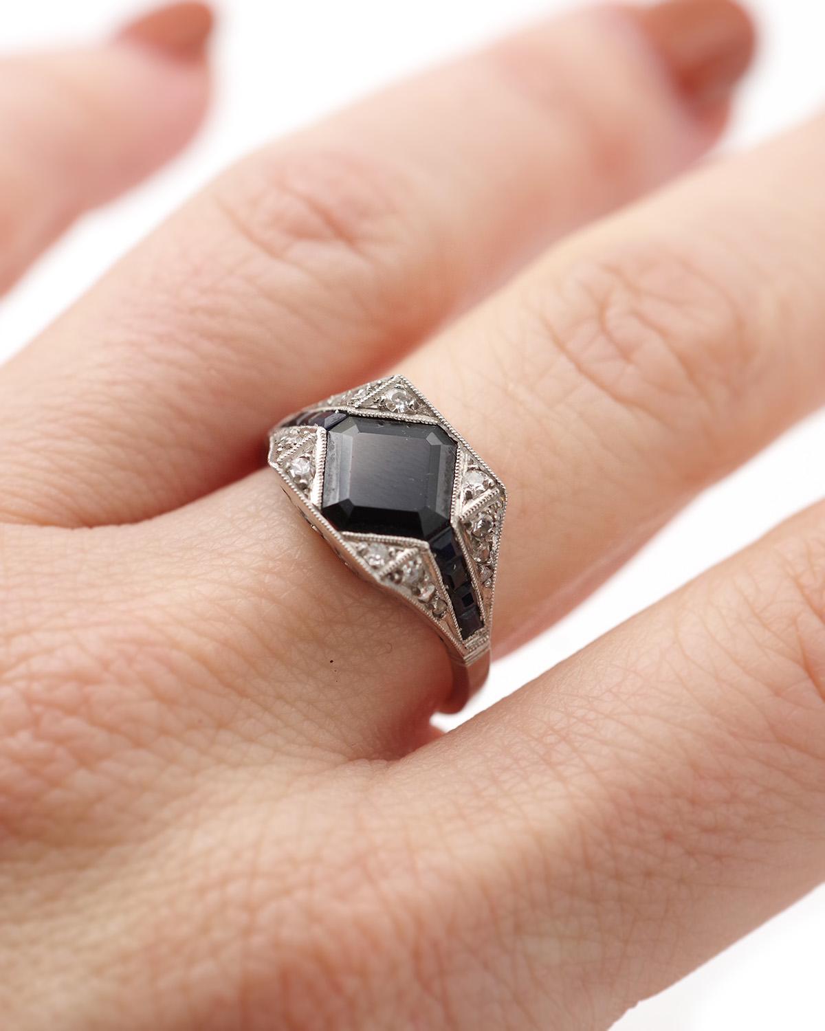 Bague Art déco en saphir en forme de losange en platine. La bague présente des formes géométriques centrées sur un saphir bleu foncé de 1,72 ct de taille carrée. Les coins sont sertis de saphirs calibrés qui se prolongent sur les épaules du