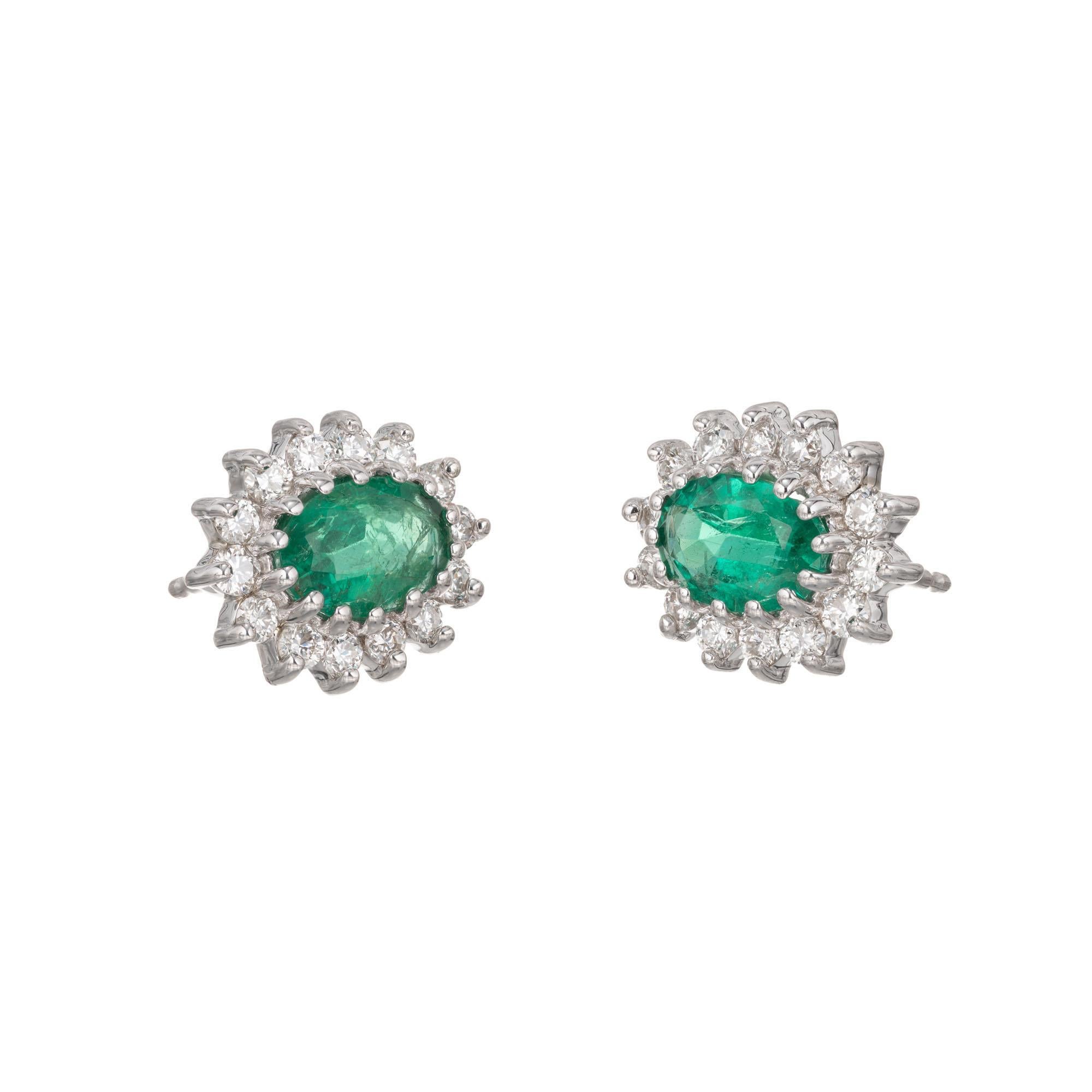 Green oval emeralds with a halo of round full cut diamonds, in 18k white gold. 

28 round full cut diamonds, approx. total weight .56cts, G, VS
2 oval top fine bright gem green oval Emeralds 7 x 5mm, approx. total weight 1.75cts
18k White