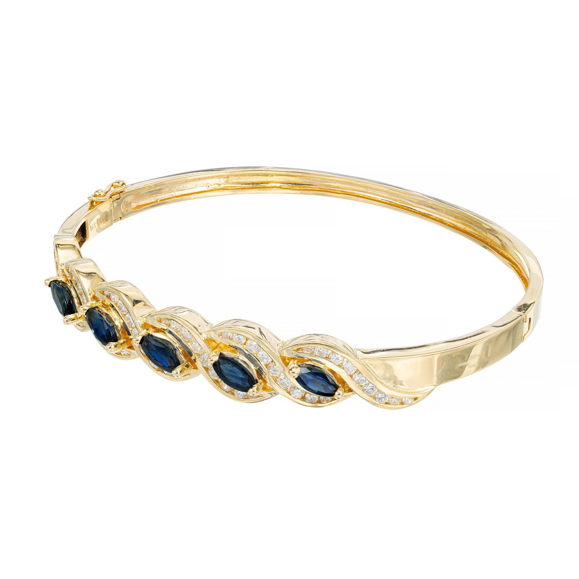 Sapphire and diamond bangle bracelet. 5 marquise slant set sapphires totaling 1.75cts are mounted in a 14k yellow gold bracelet, with a swirl design halo of 54 round cut diamonds. This bangle is hinged with a figure 8 safety clasp. 

5 marquise blue
