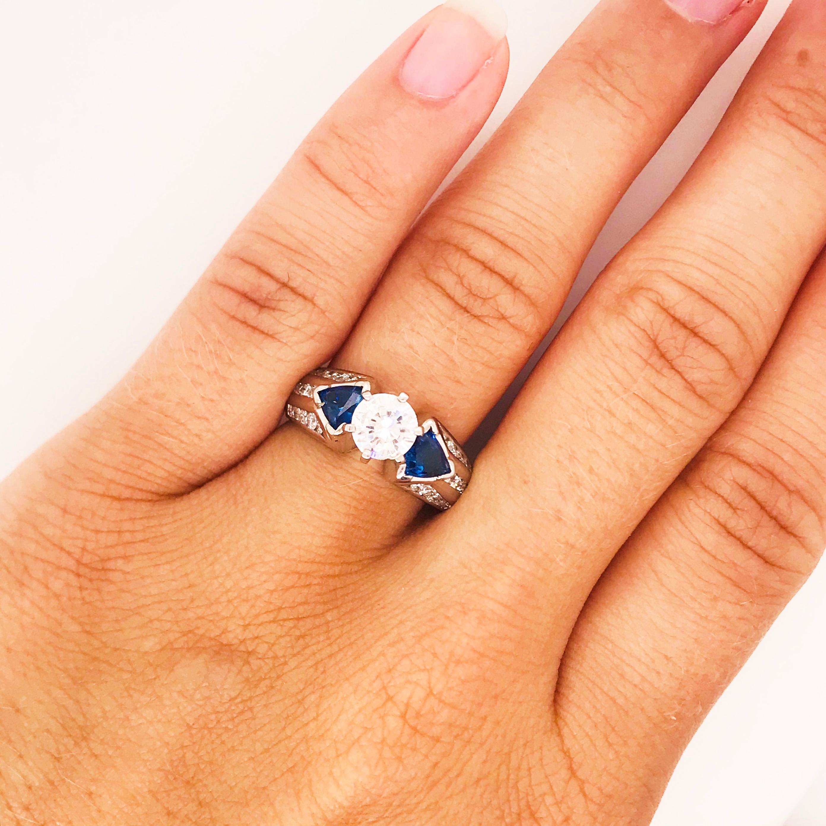 Blue, bold and beautiful! This gorgeous, timeless custom engagement ring has a round brilliant diamond center that is exactly 1.00 carat total weight! The diamond is bright white and eye clean! The engagement ring has a trillion, genuine blue
