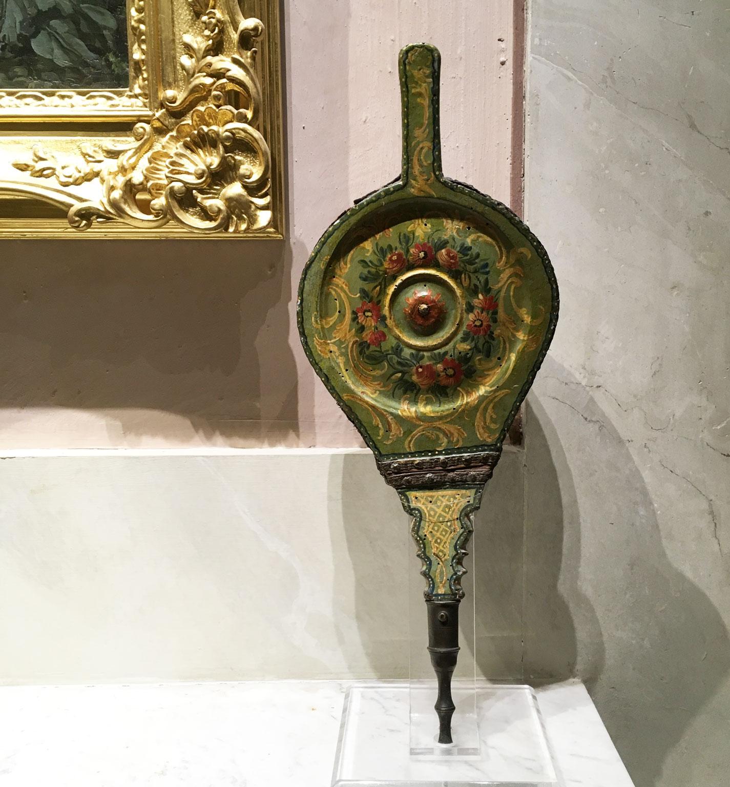 Se trata de un raro fuelle de chimenea de madera tallada y lacada con decoraciones polícromas de flores sobre fondo verde claro. Tiene detalles originales de cuero y el pitorro de bronce.  Esta elegante pieza procede de mediados del siglo XVIII, de