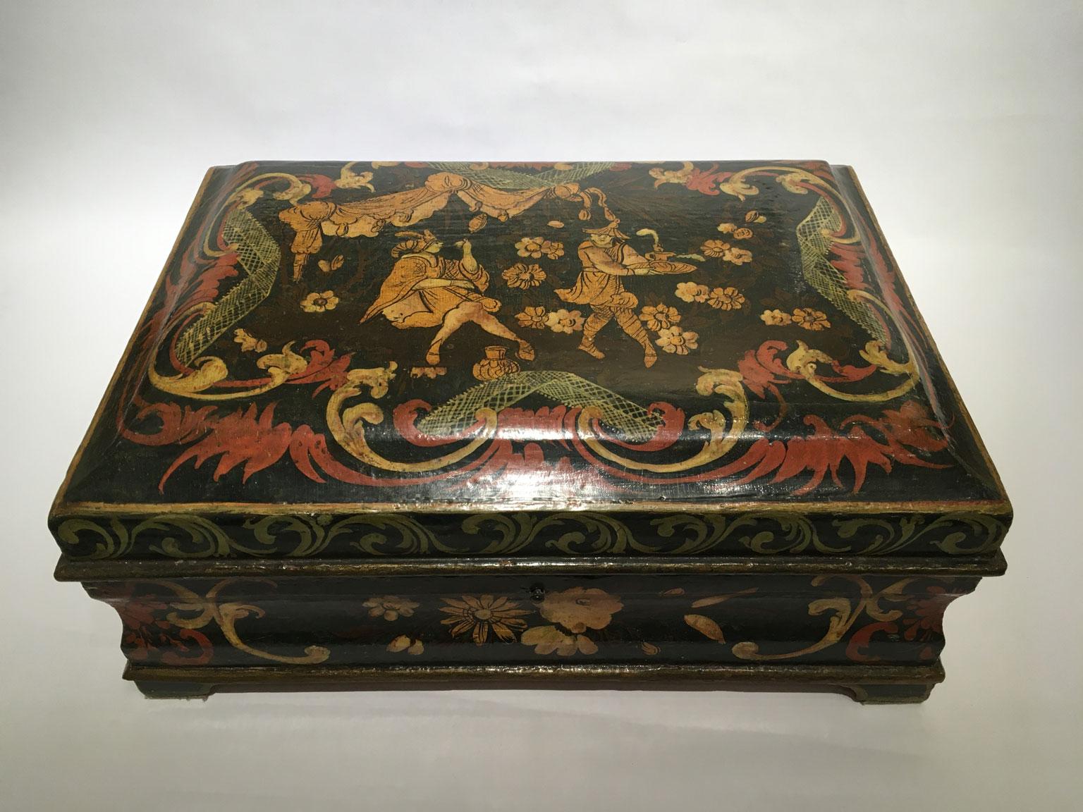 Se trata de una refinada y exquisita caja de madera lacada, con decoración policromada y dorada sobre fondo azul oscuro. El color azul oscuro podría parecer un verde oscuro. En la tapa volutas de color rojo brillante y marfil con inserciones de