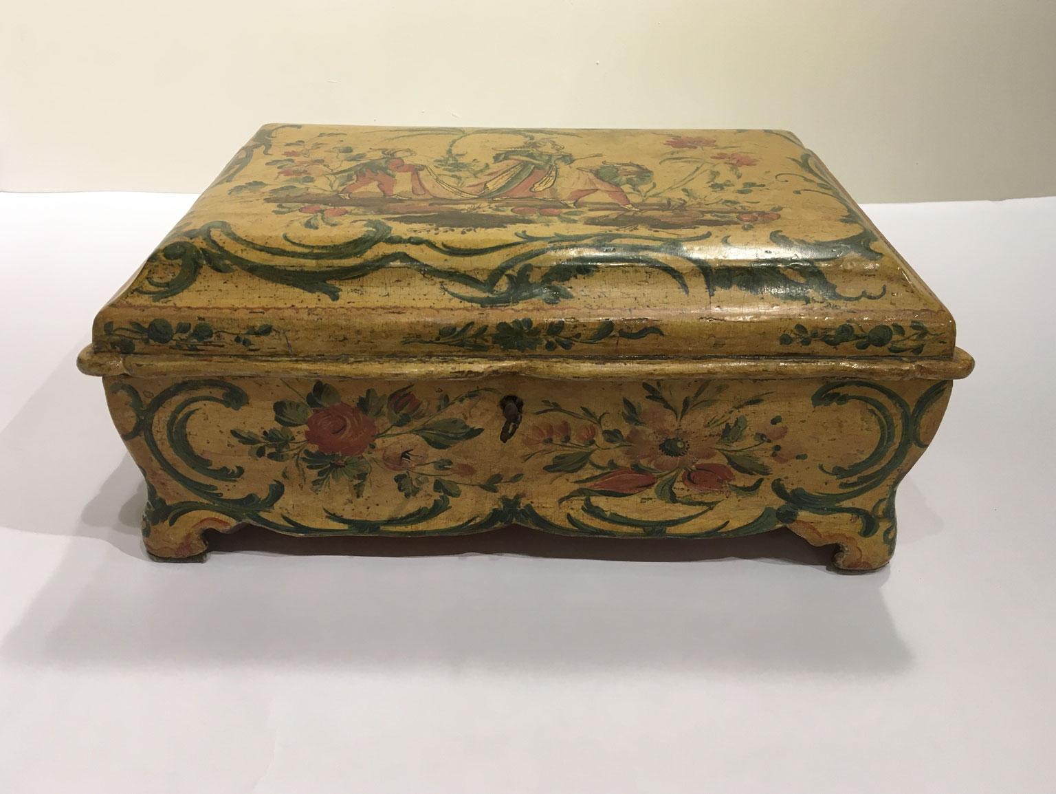 Se trata de una magnífica caja de madera lacada, con una rica decoración policroma sobre fondo amarillo.
En el centro de la tapa se ha pintado un paisaje exótico con palmeras, flores y bayas que rodean la figura de la dama elegantemente vestida.
La