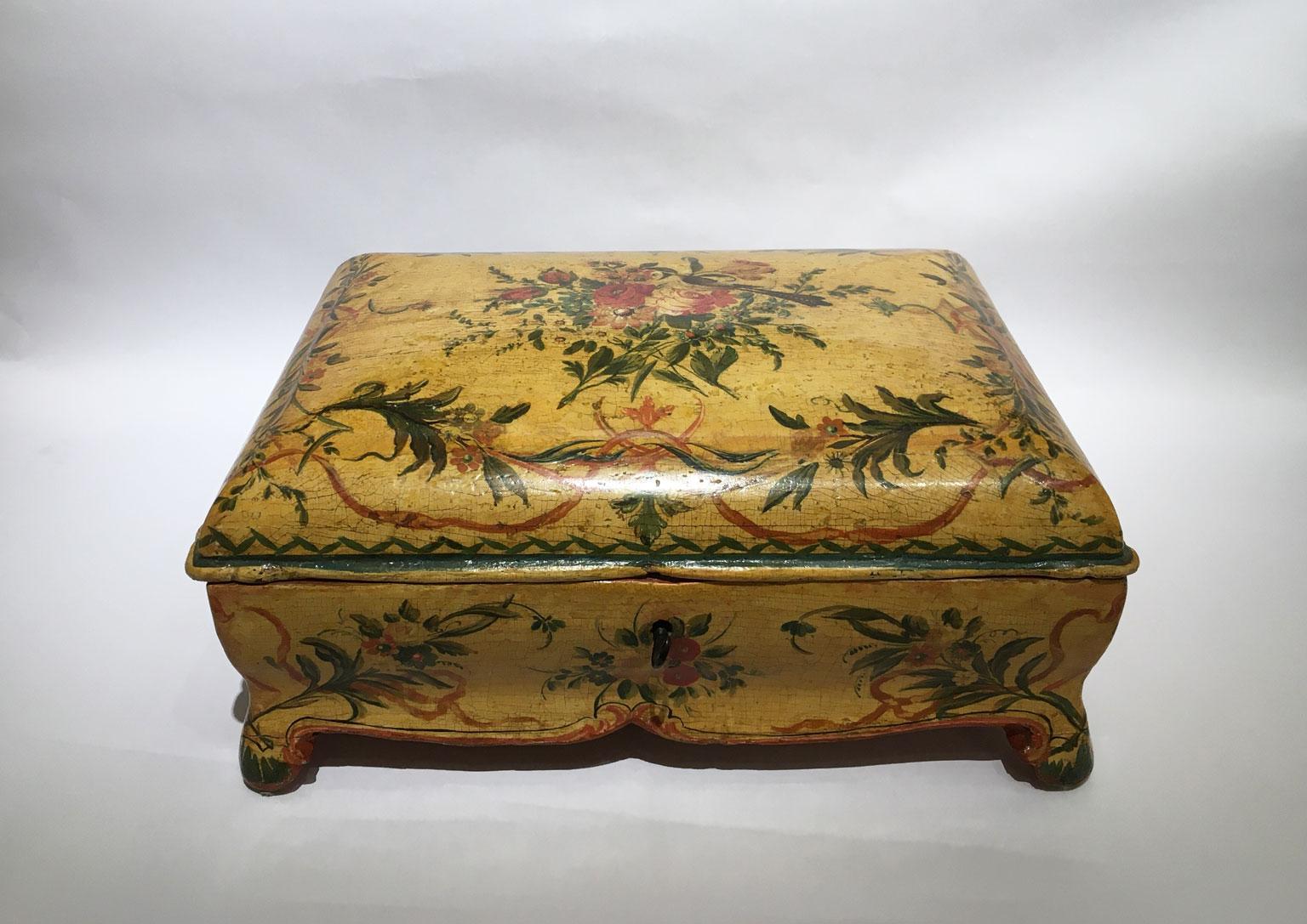 Il s'agit d'une élégante boîte en bois laqué et façonné, avec un décor de fleurs fines et polychromes sur fond jaune. Au centre du couvercle, un bouquet de fleurs a été peint et sur le dessus de celui-ci, repose un petit oiseau à la longue queue