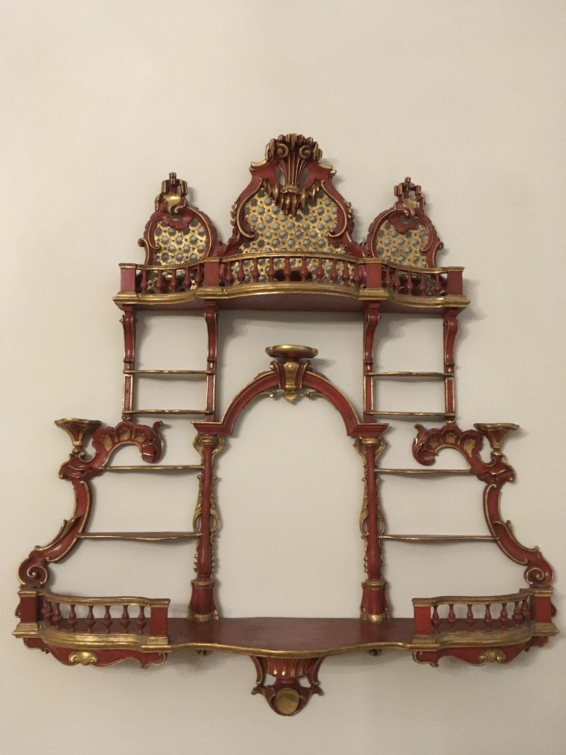 Il s'agit d'une exquise et rare étagère en bois sculpté, gravé et laqué rouge et d'un support en porcelaine, avec des détails dorés. Façonné avec des perspectives architecturales, avec des étagères et des marches dégradées. De la balustrade