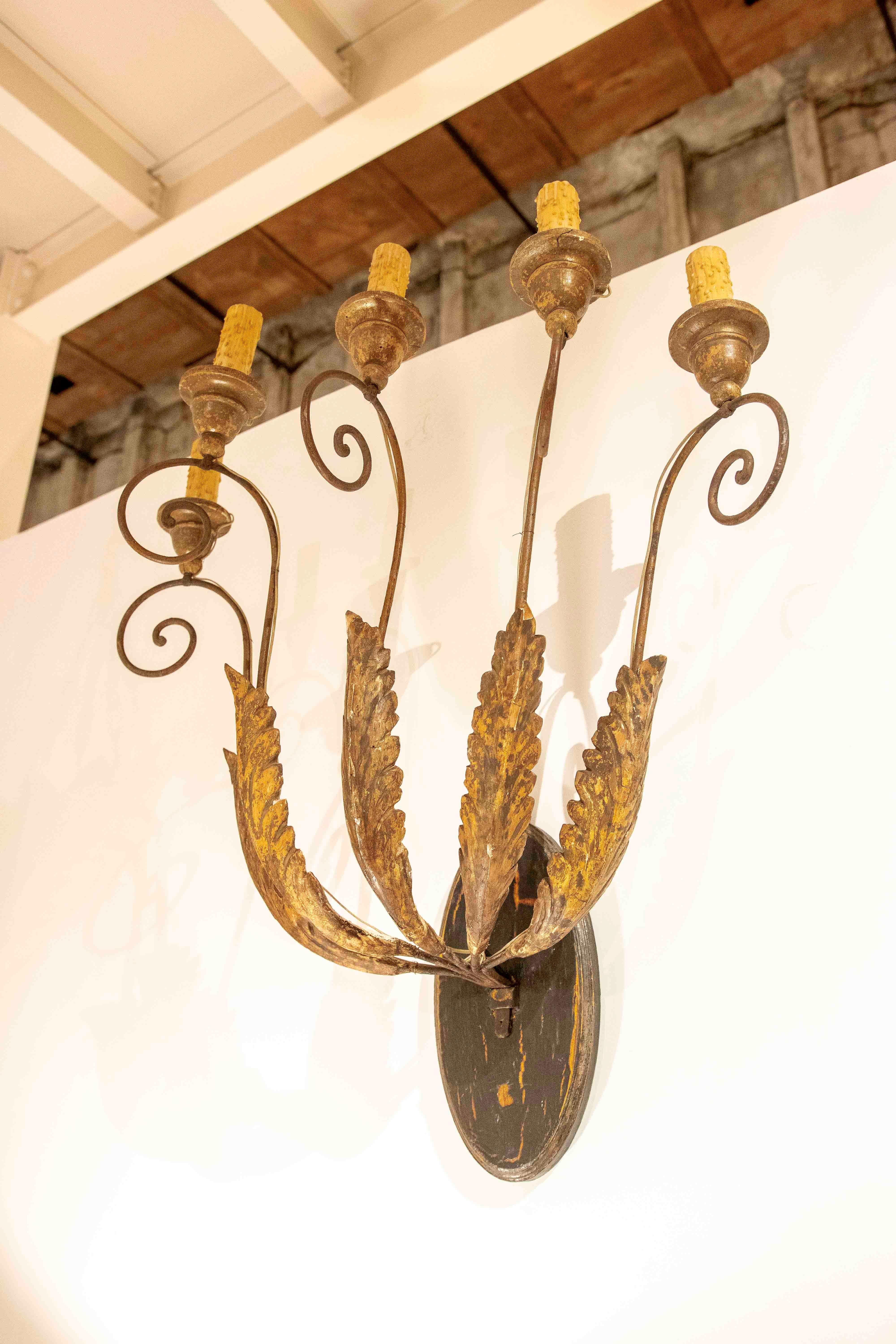 Set of two wall sconces made of wrought iron and wooden leaves with stuco, designed with three candle holders each and decorated with details of leaves and curves. These pieces are ideal for adding a unique touch to interior spaces, offering