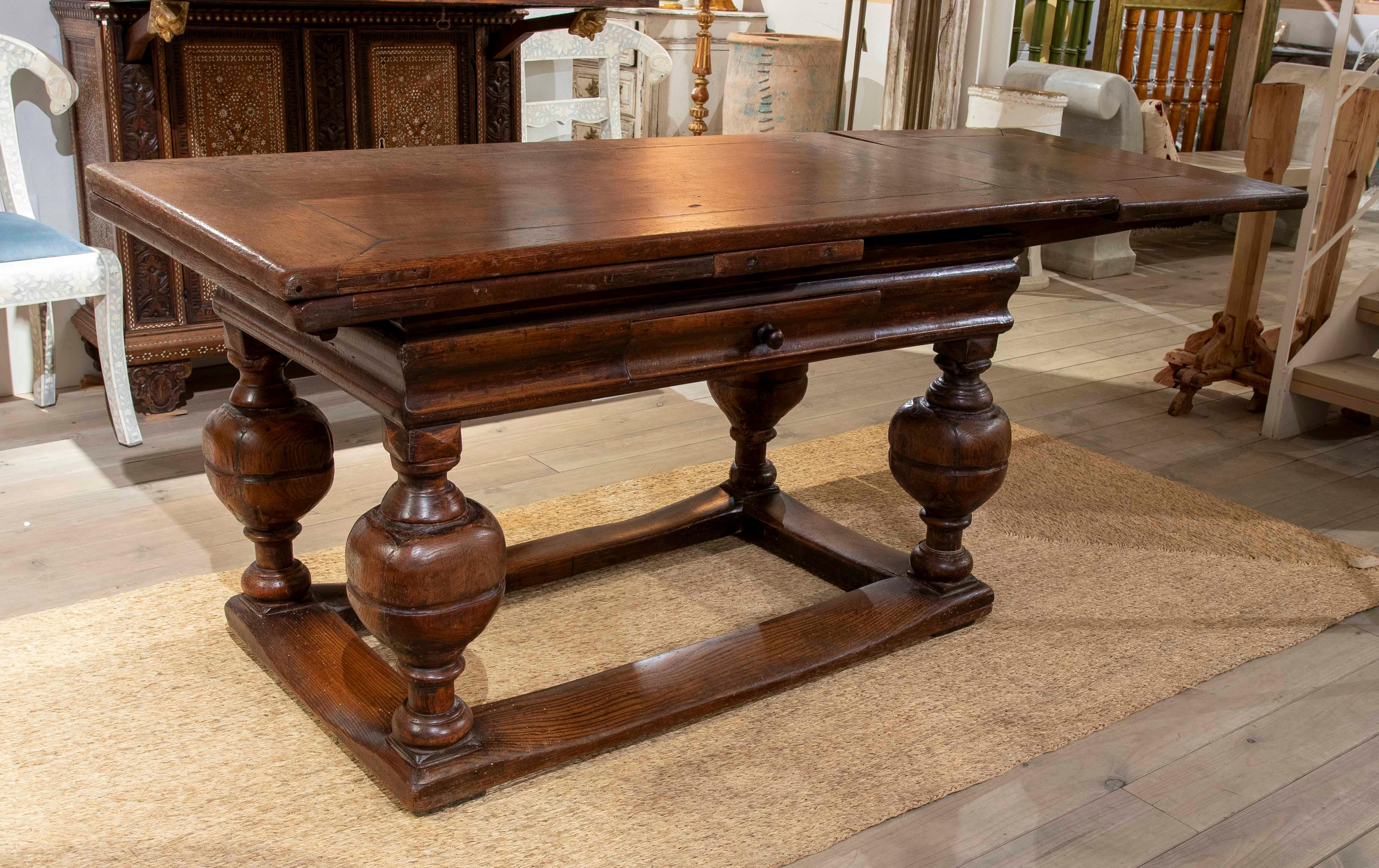 The table's open width is 261 cm.

This impressive extendable table is crafted from solid oak, with a design that combines functionality and classic elegance. The piece features a solid structure with four large, turned legs, joined by an H-shaped