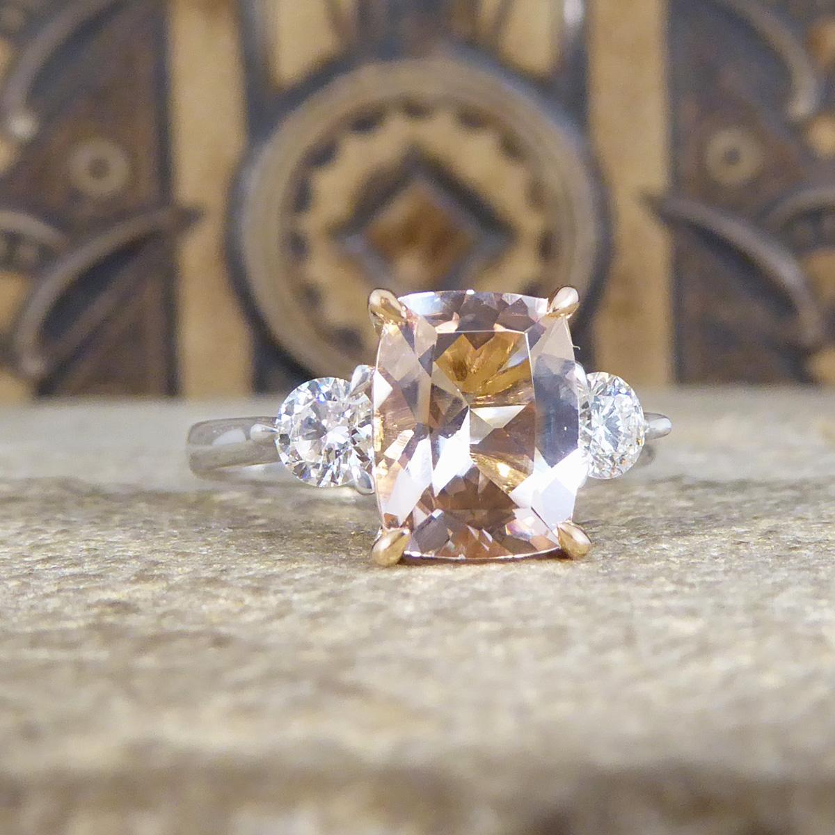 An absolutely gorgeous and sparkly Pink Morganite and Diamond three stone ring that holds three beautiful stones set in a secure four double claw setting. In the centre sits a lovely bright Cushion Cut Pink Morganite in the centre weighing 1.75ct