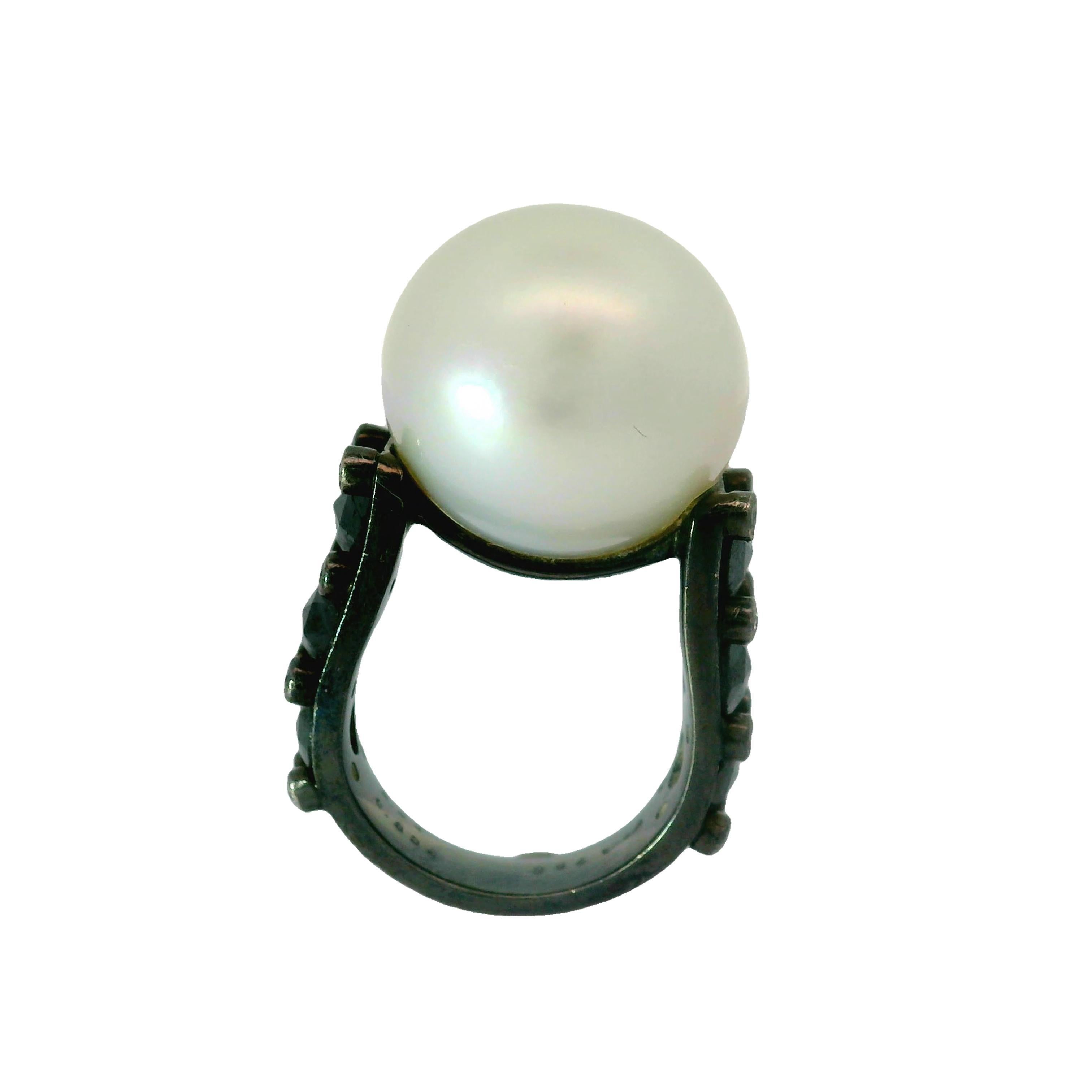 A striking South Sea Pearl, measuring an impressive 17.5 millimeters, is the focal point of this contemporary ring. The pearl's smooth, white surface exudes a natural luster which makes the pearl glow in the light. Accentuating the pearl are black