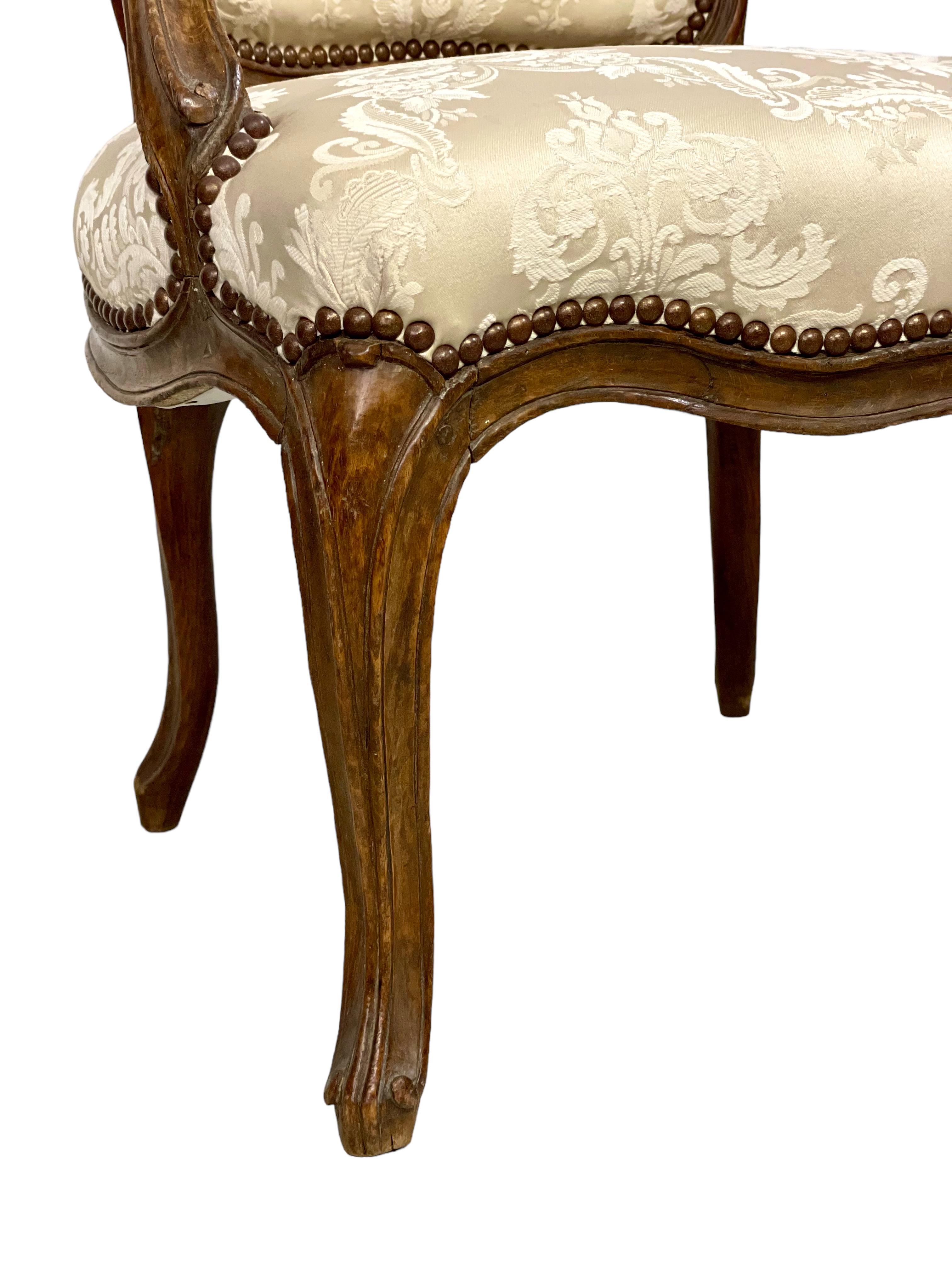 A luxurious Louis XV period armchair in beautifully carved and moulded walnut, with ornate scroll-carved arm rests and supports. This elegant 'Fauteuil à la Reine' dates from the 18th century, and has a padded, slightly inclined back and overstuffed