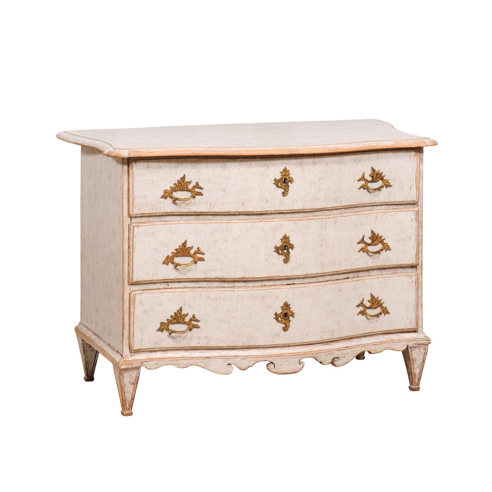 A Swedish Rococo period painted chest from circa 1760 with three drawers, ormolu hardware, light gray / cream painted finish, serpentine front and carved skirt. Emanating the poetic allure of the Rococo era, this Swedish chest from circa 1760 is an