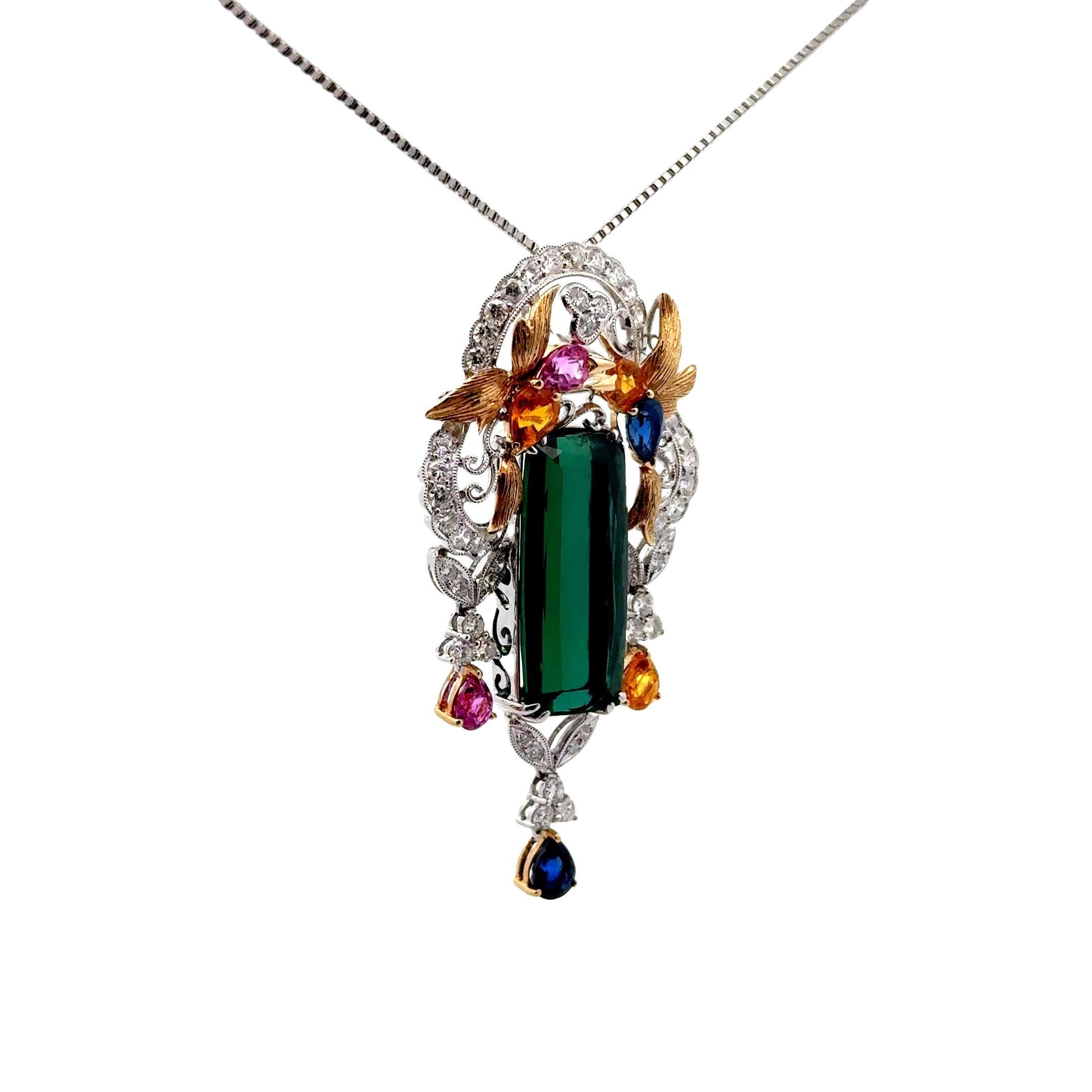 This exquisite pendant, which doubles as a brooch, features a 17.63 carat cushion-cut elongated tourmaline at its center, radiating a deep vivid slightly bluish-green color. Crafted with intricate detail, the design incorporates a floral motif with
