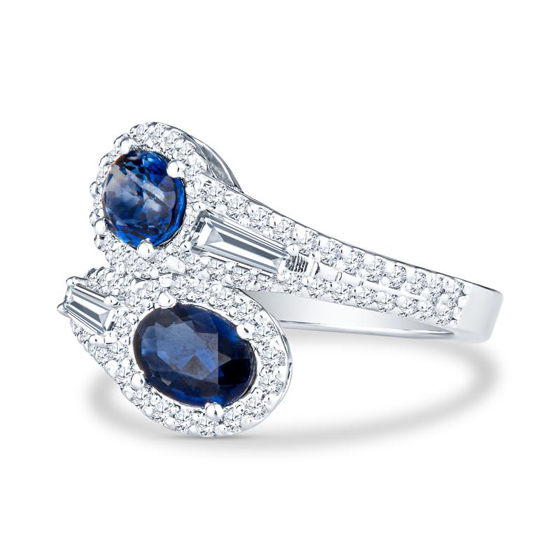 This unique bypass ring features 1.76 carat total weight in oval cut natural blue sapphires accented by 0.88 carat total weight in baguette and round diamonds set in 14 karat white gold. It is a size 6.5 but can be resized upon request.