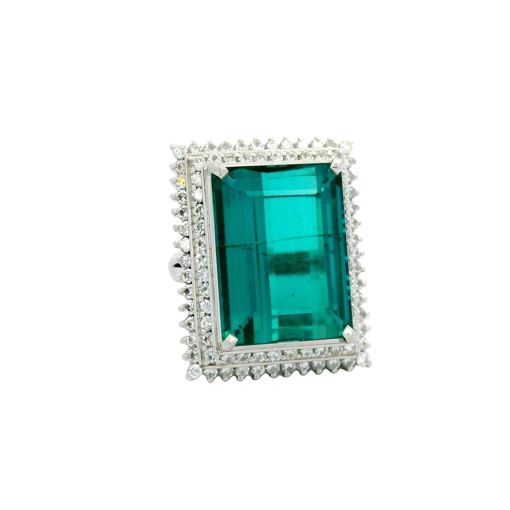 Un'affascinante tormalina indicolite, del peso di ben 17,79 carati, è il centro di questo anello contemporaneo. La pietra dal taglio smeraldo è incorniciata da un'aureola di diamanti bianchi rotondi, per un totale di 1,41 carati, che ne esaltano la