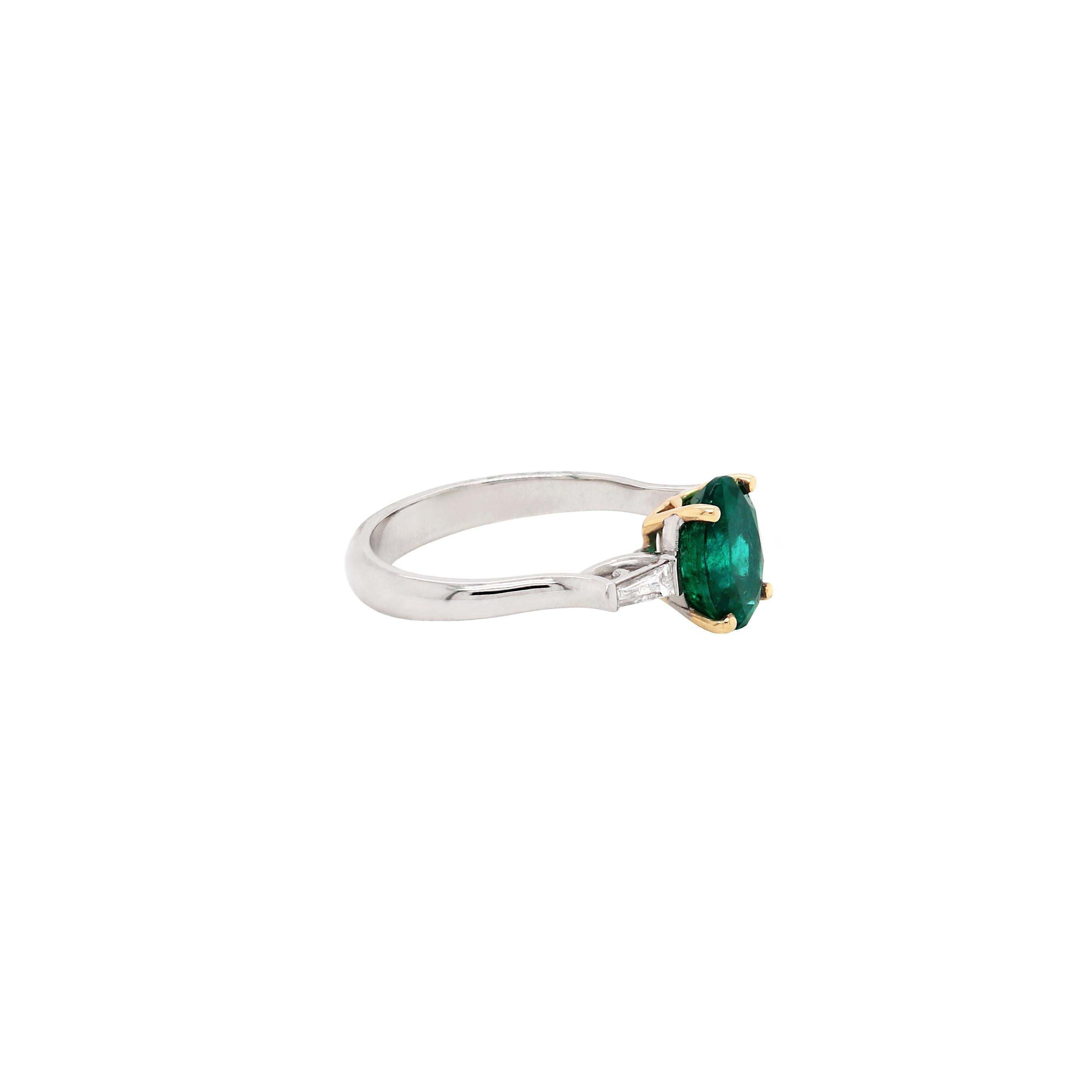 This ring features a natural oval shaped emerald weighing 1.77ct in an 18 carat yellow gold four claw, open back setting. The beautiful emerald is accompanied by a fine quality tapered baguette diamond on either side with a total diamond weight of