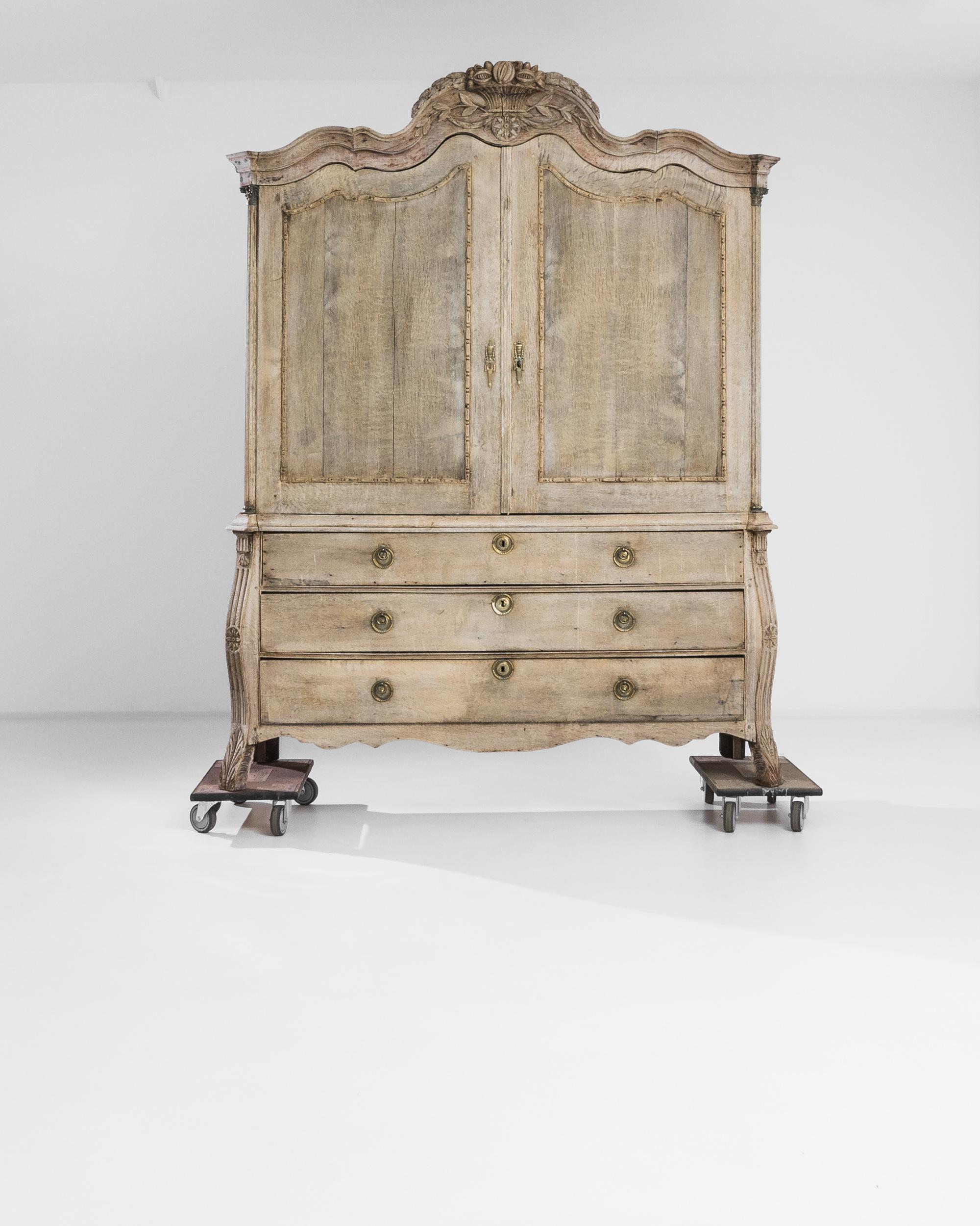 An antique oak cabinet with a beautiful Silhouette. Made in the Netherlands in the 1780s, the scalloped cornice lends the case a sinuous shape; a carved cornucopia of fruit, nuts and flowers, wreathed with laurel leaves, provides a crowning detail.