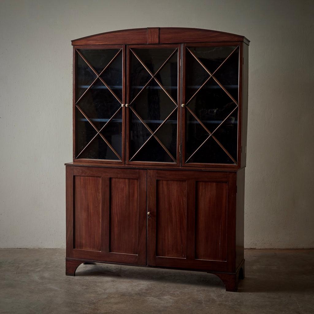 English 18th-century Hepplewhite mahogany bookcase with beautiful clean lines and pleasing proportions. The arched top features a small panel accent, and frames three mahogany X-patterned glass paneled doors with round brass handles. This upper