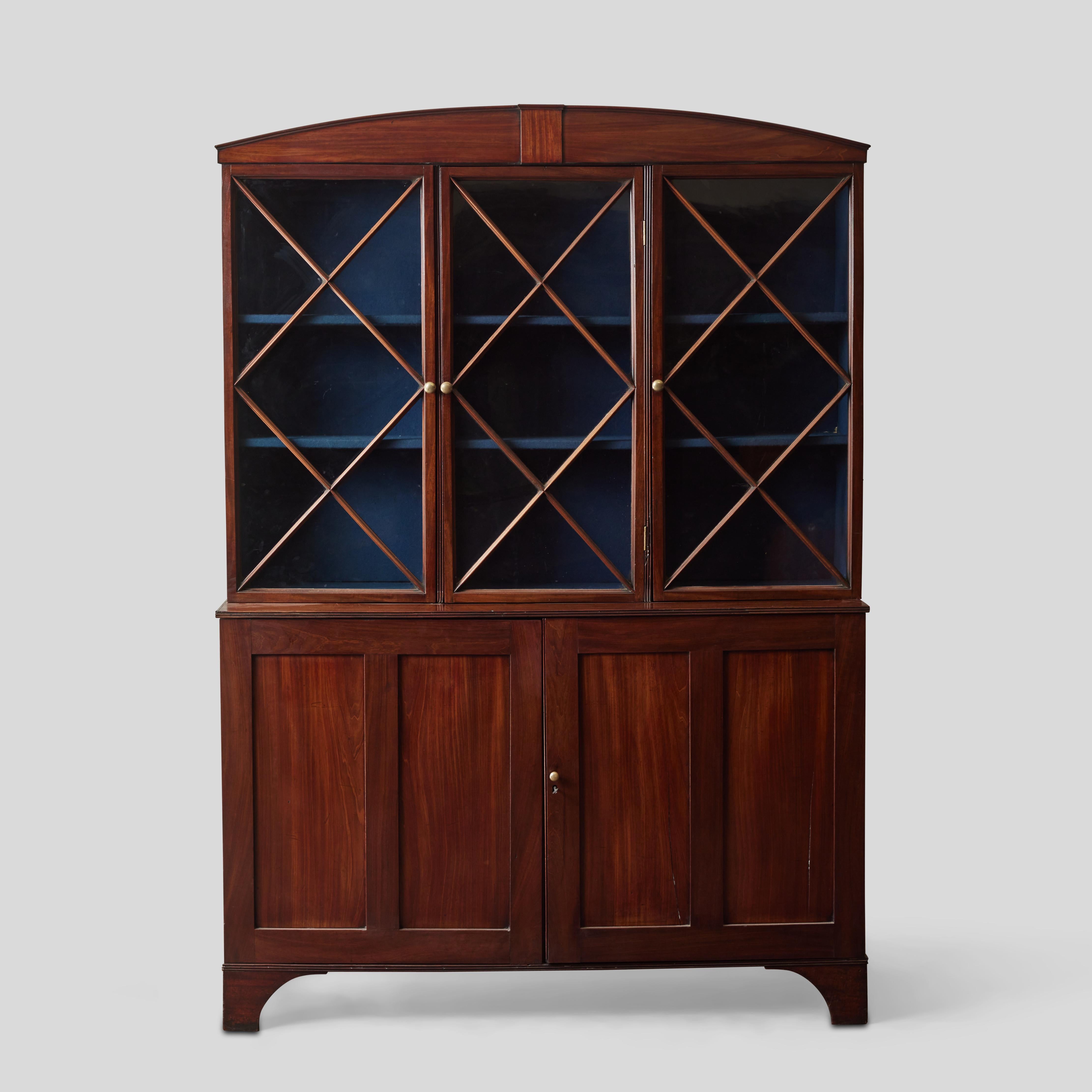 English 18th-century Hepplewhite mahogany bookcase with beautiful clean lines and pleasing proportions. The arched top features a small panel accent, and frames three mahogany X-patterned glass paneled doors with round brass handles. This upper