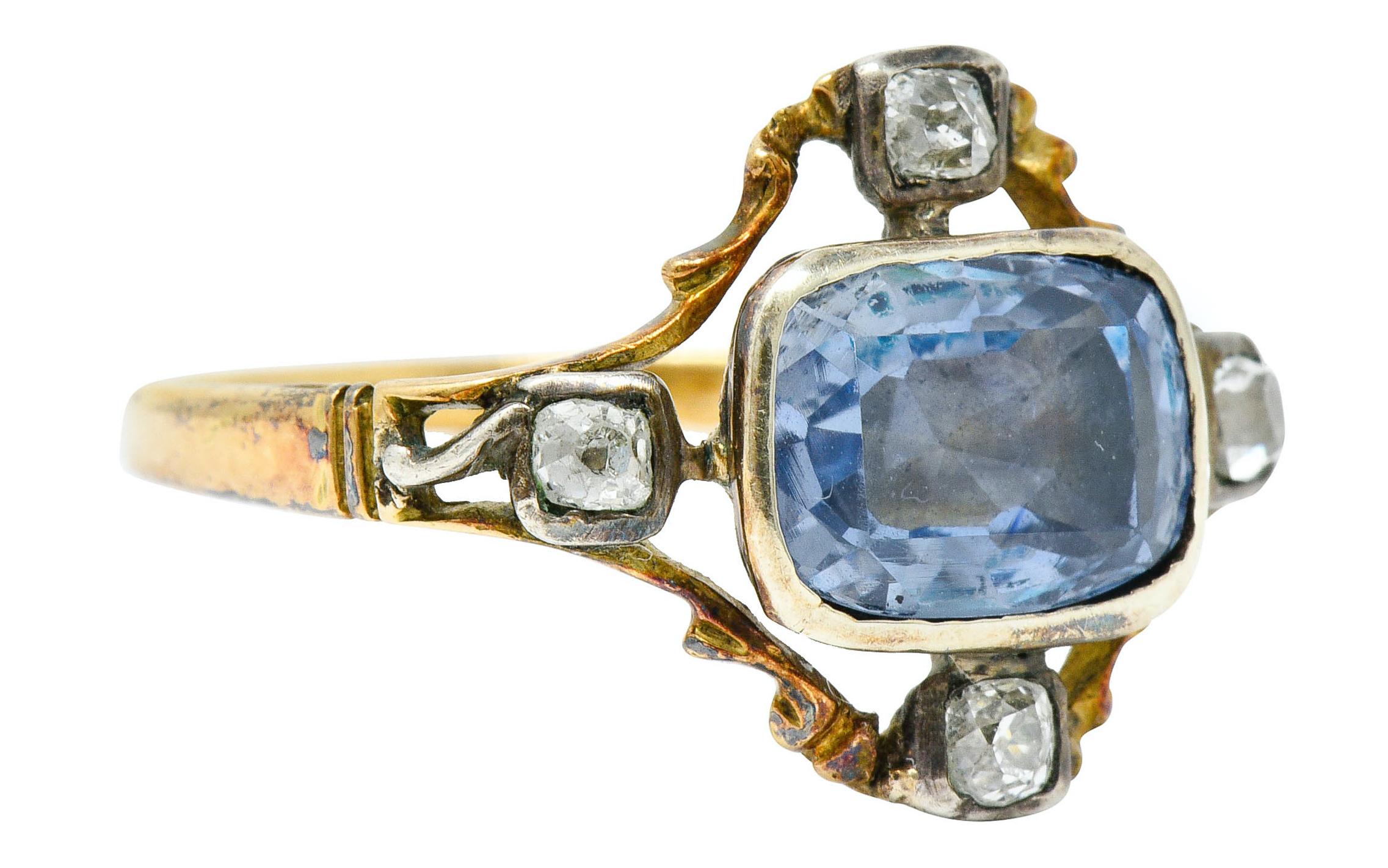Centering a rectangular cushion cut sapphire weighing approximately 2.00 carats

Transparent with light blue color and foil backing that does not alter light blue color

Surrounded by old mine and old single cut diamonds at each cardinal point

Set