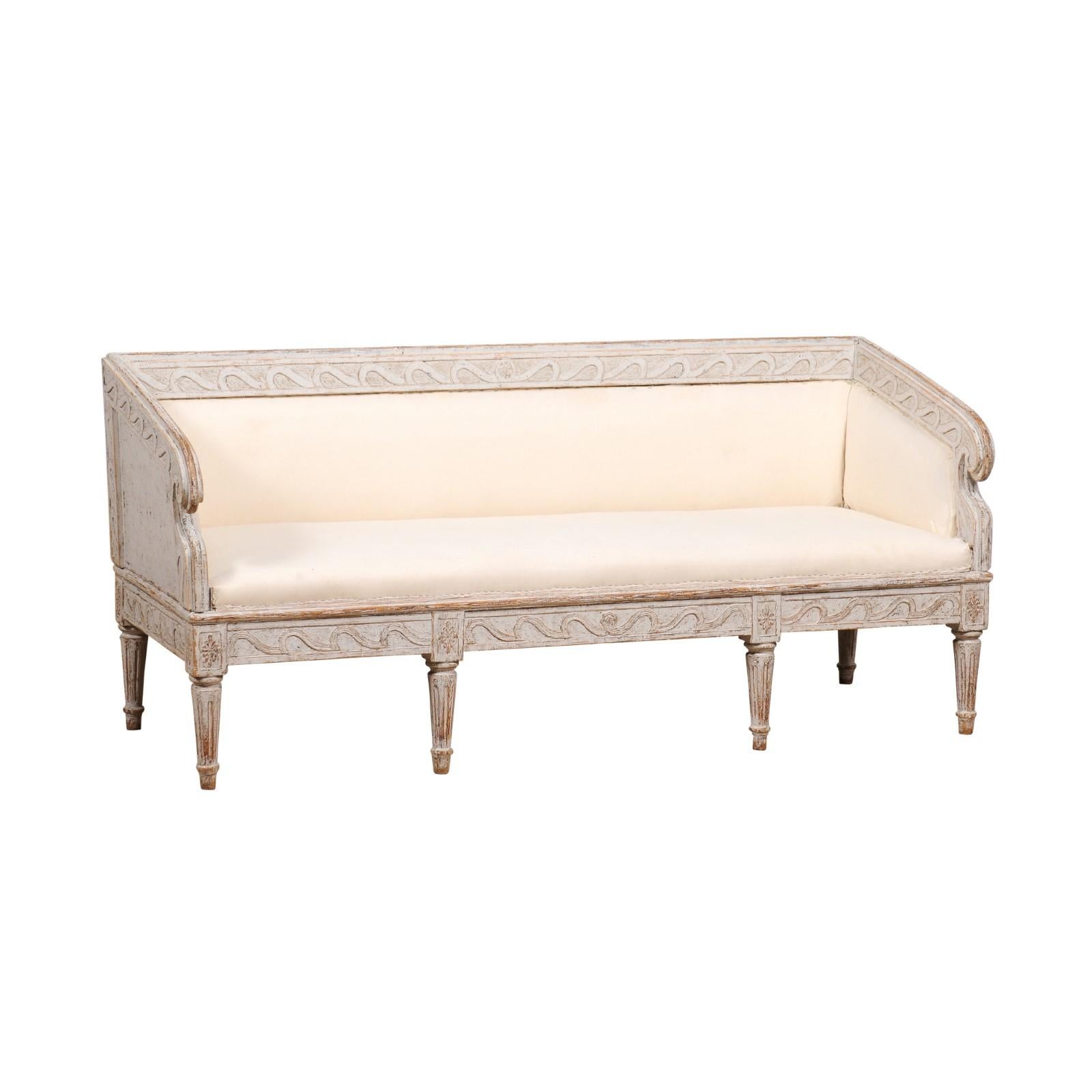 A Swedish Gustavian period sofa from circa 1780 with carved Vitruvian scroll inspired friezes, rosettes, fluted legs and classic light gray painted finish. A breathtaking embodiment of Swedish Gustavian elegance, this circa 1780 sofa is a veritable