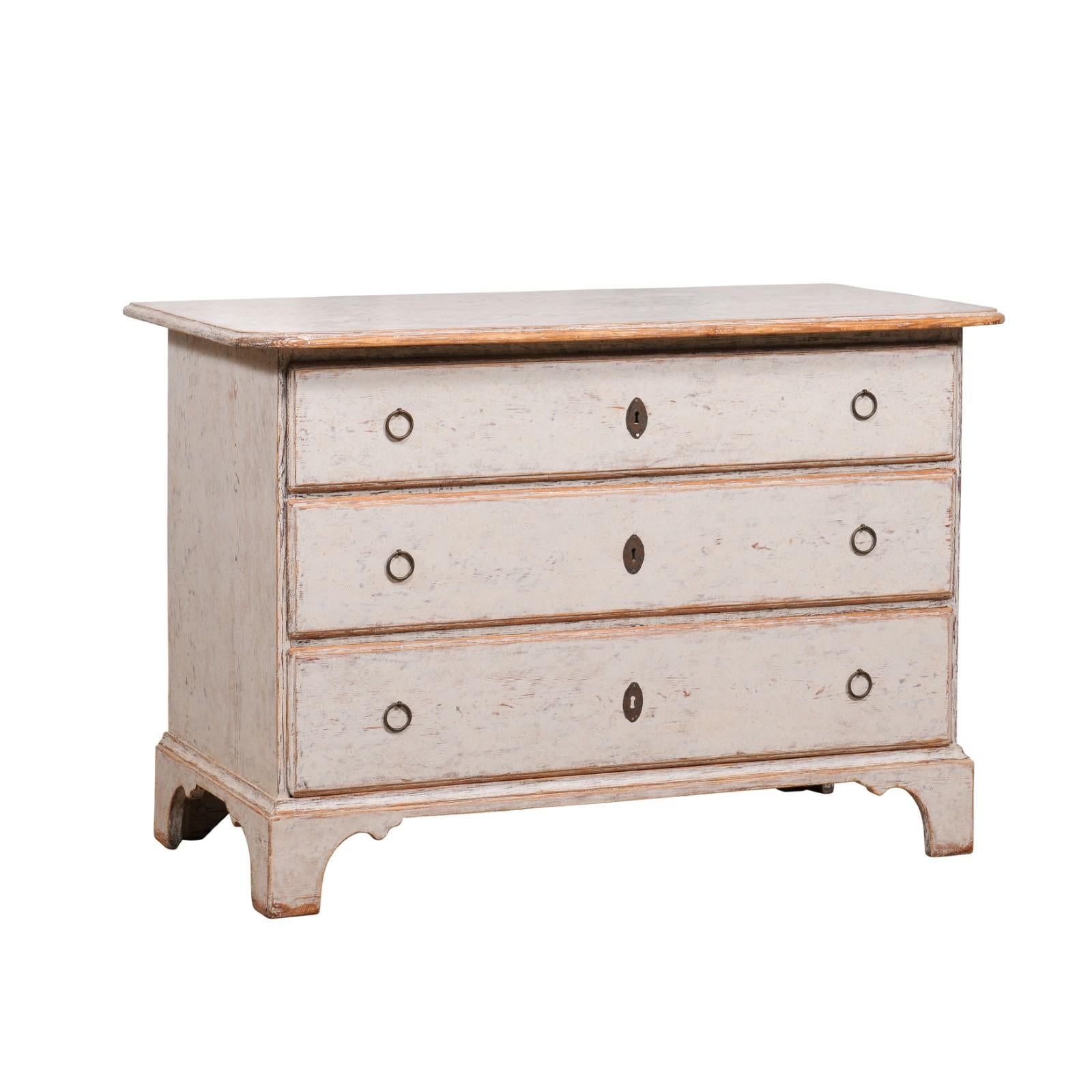 A Swedish light gray painted chest from circa 1780 with three drawers and carved bracket feet. Captivating in its understated elegance, this Swedish Chest from circa 1780 offers a seamless blend of functionality and style. Swathed in a light gray