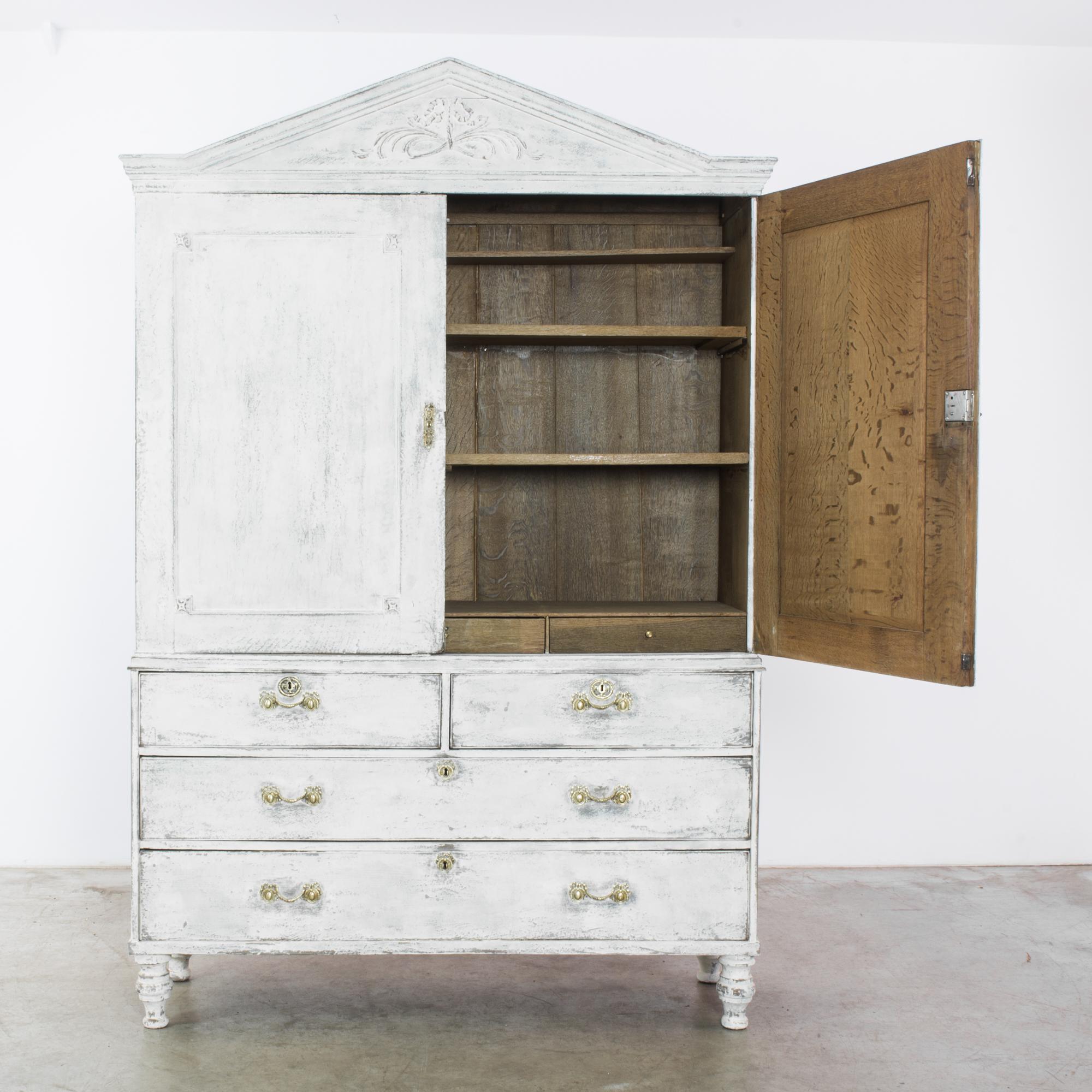 This two-part eighteenth century wooden armoire with shelves resting on a chest of drawers was made in Belgium. Its peaked top and delicate ornamentation evoke a sense of romanticism. The decorative pulls and locks, paneling details, and carved