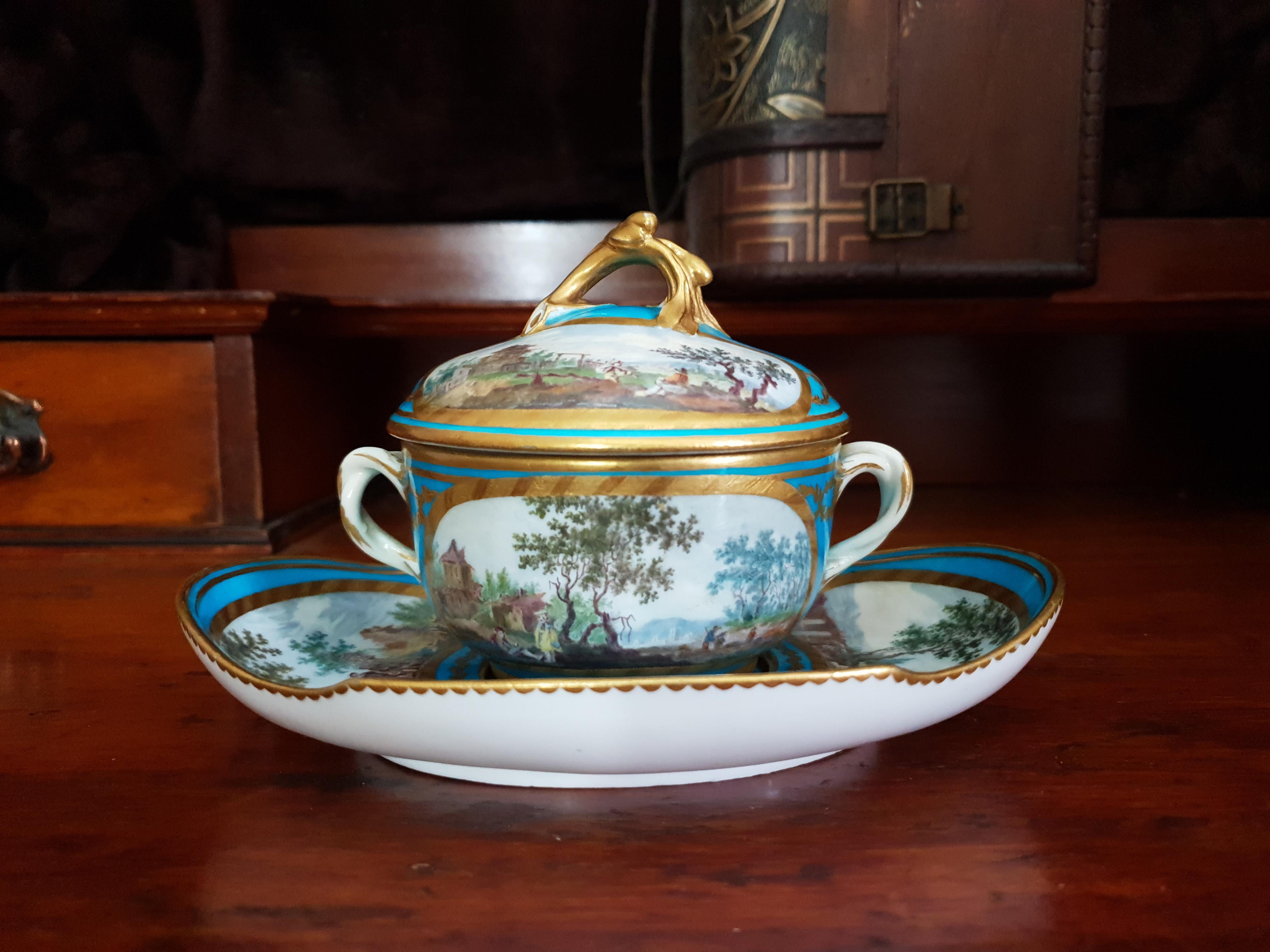 Superb Sevres turquoise collectable lidded chocolate cup and saucer with hand painted scenes of nature. An acanthus moulded gilt handle sits atop the lid with two vignettes of hand painted scenes of nature on either side of the handle. On either