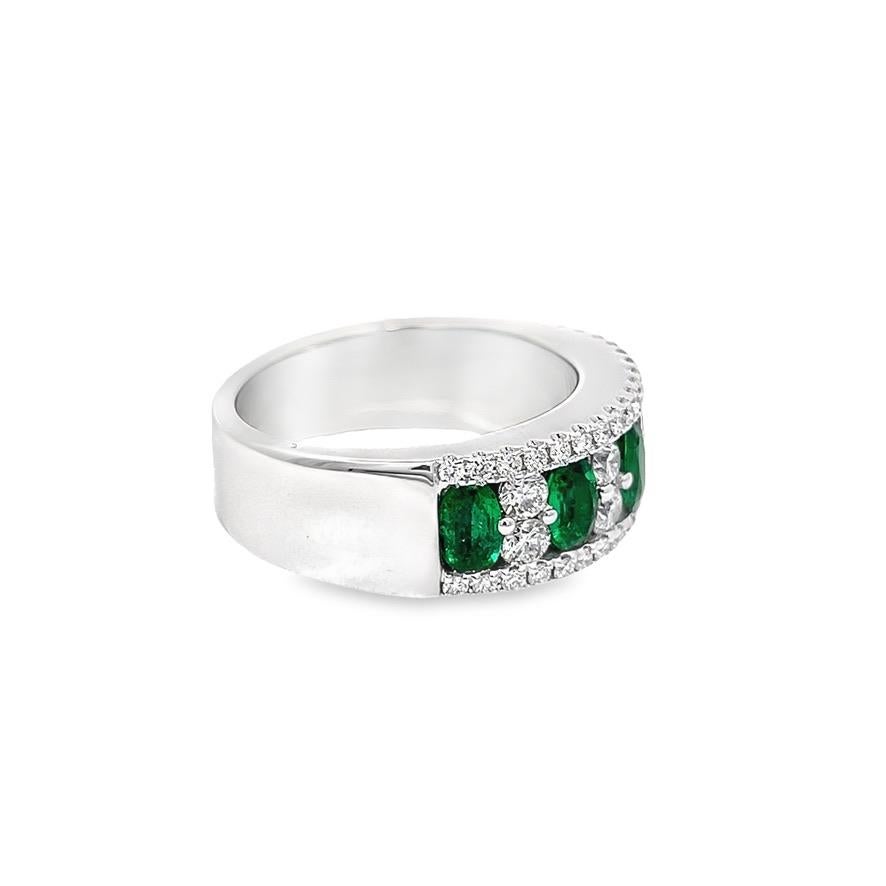 Exuding 5 beautiful oval-cut natural emeralds gemstones bordered by brilliant round diamonds in this distinctive women's anniversary ring inspired on the late victorian style. Fashioned in 18K white gold, the total diamond weight of the ring is 0.80