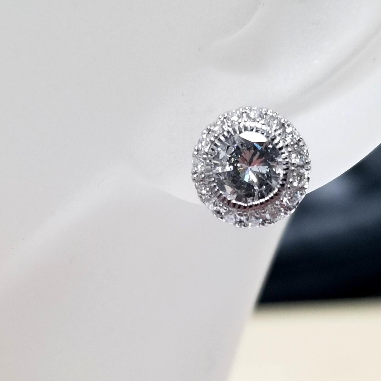 Cette magnifique paire de boucles d'oreilles est fabriquée en or 14 carats avec une paire de diamants ronds brillants sertis en chaton d'un poids total de 1,45 ct au centre (4,3 mm) d'un halo pavé de 30 diamants ronds brillants de 1,3 mm. Les bagues