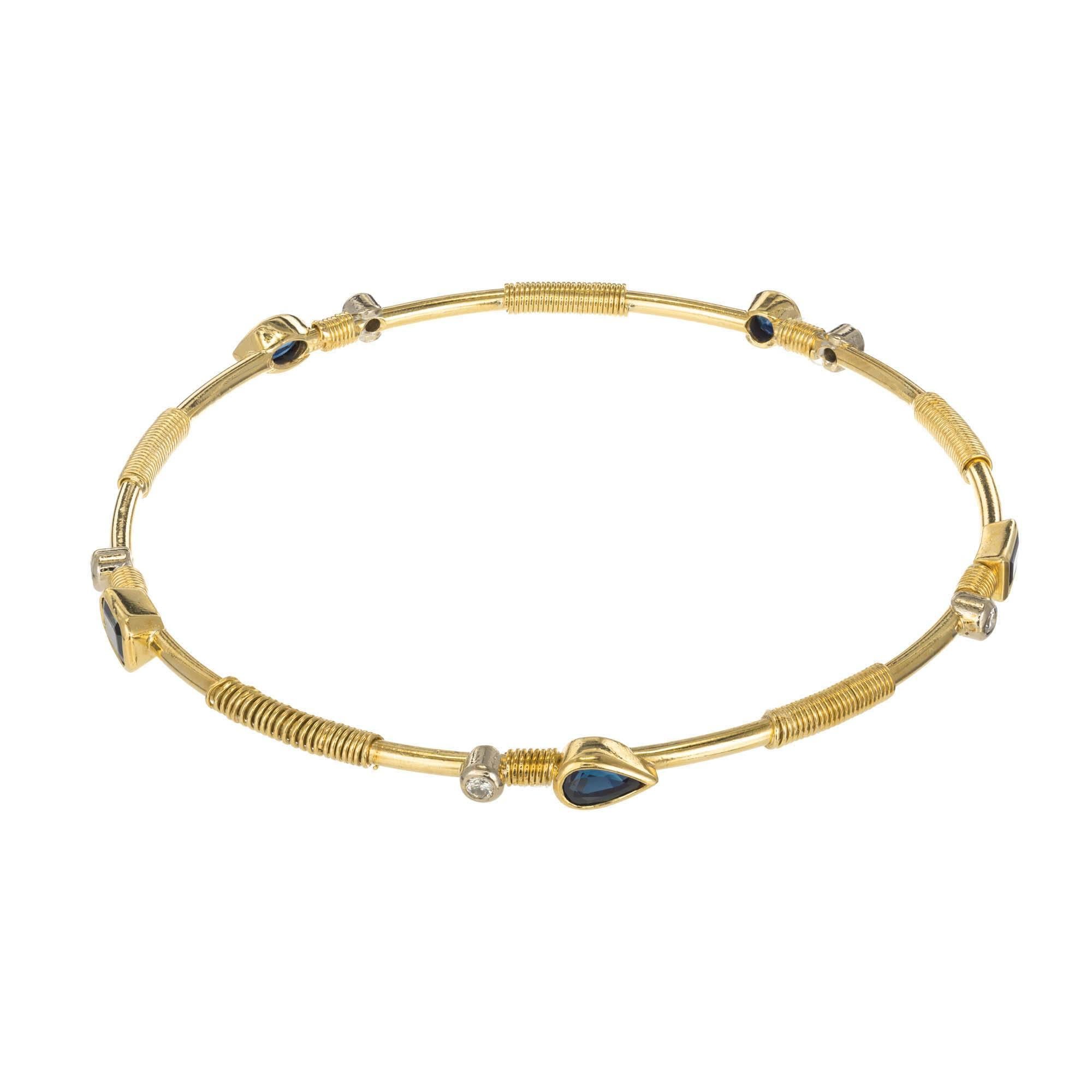 22k yellow gold bangle set with bezeled sapphires varying shapes and round diamonds with a coil wire design between stones.

1 round sapphire 3.5 x 2.2 mm Approximate .18 carats
1 marquise sapphire 5.0 x 4.0 x 2.9 Approximate .54 carats
1 pear