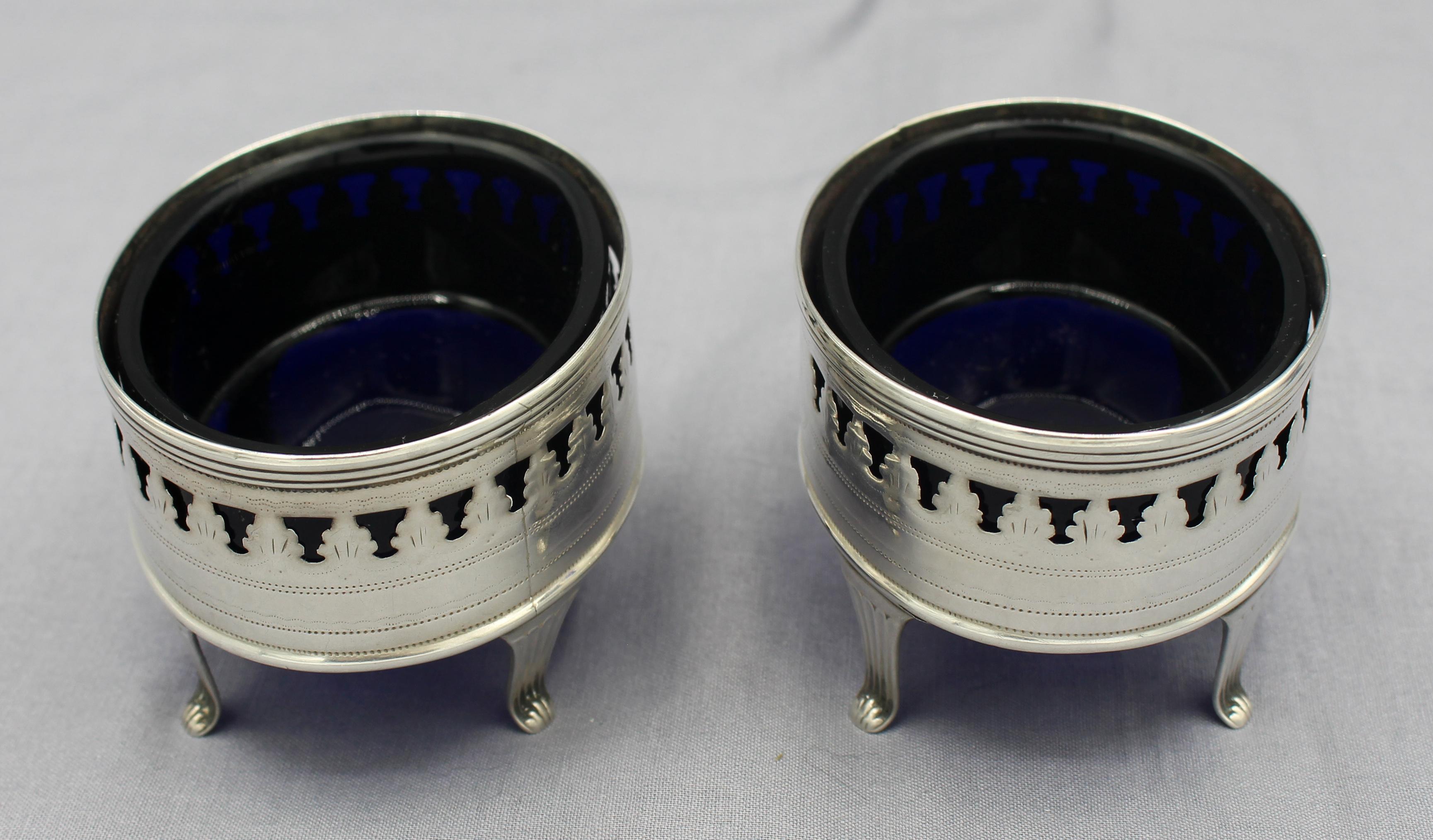Pair of sterling silver oval master salts by Peter & Ann Bateman, London, 1797. Cobalt glass liners. Elegantly pierced; neoclassical design typical of the Bateman family work. Scrolling monograms. Raised on four downswept legs to scrolled feet. Seam