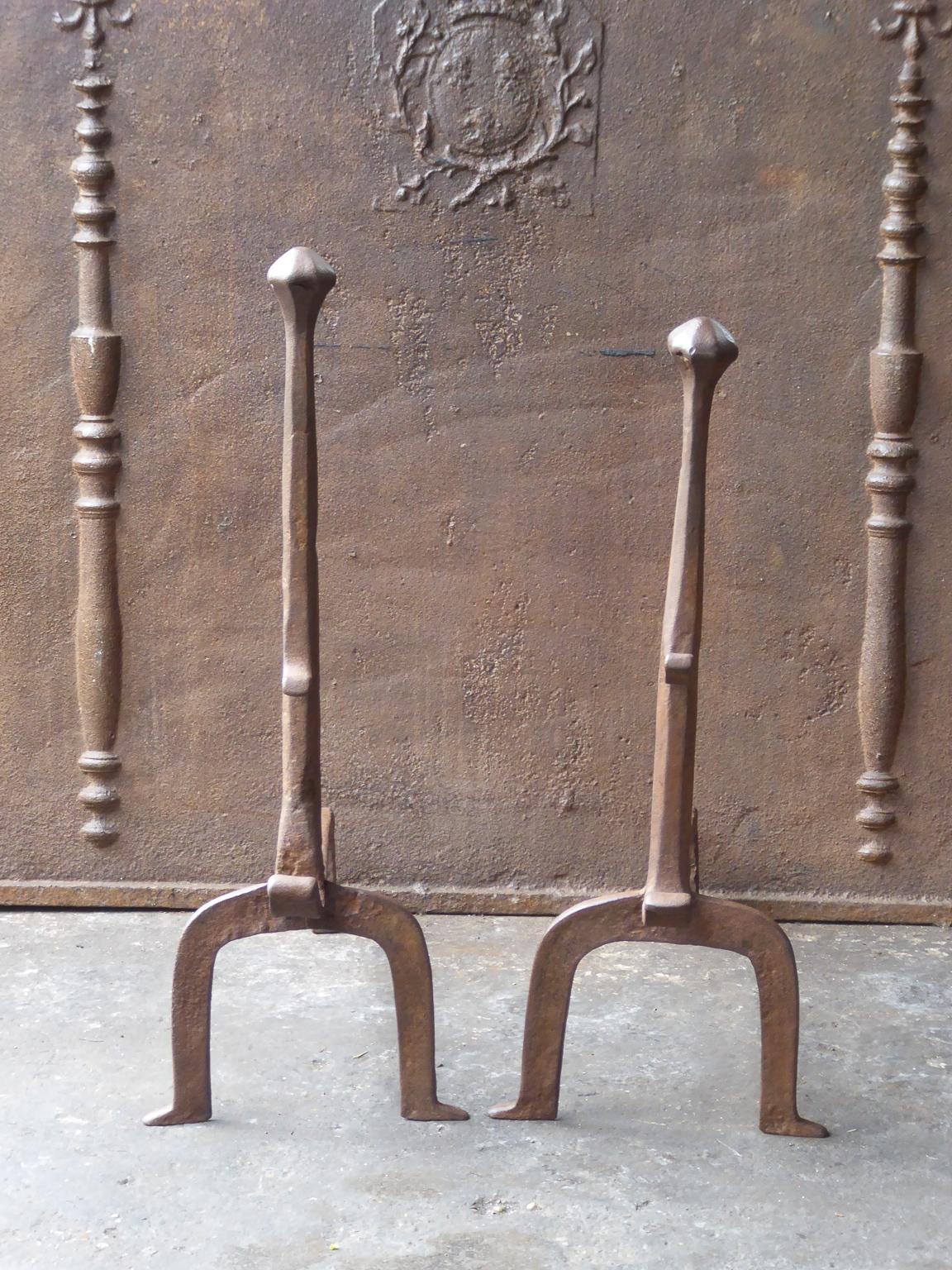 17th-18th century French andirons made of wrought iron. The style of the andirons is gothic. The andirons have spit hooks to grill food. They have a natural brown patina. Upon request it can be made black. The condition is good.