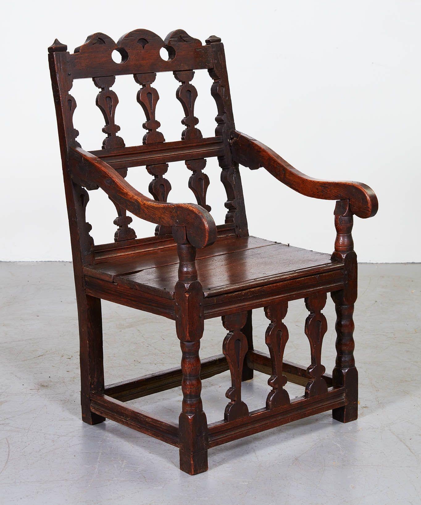 A splendid early Abbot's chair in dark bog oak with decorative back and apron of vasiform splats and fretwork railing, having shaped arms over a paneled seat and standing on bobbin legs joined by a scribed box stretcher. Impressive scale and
