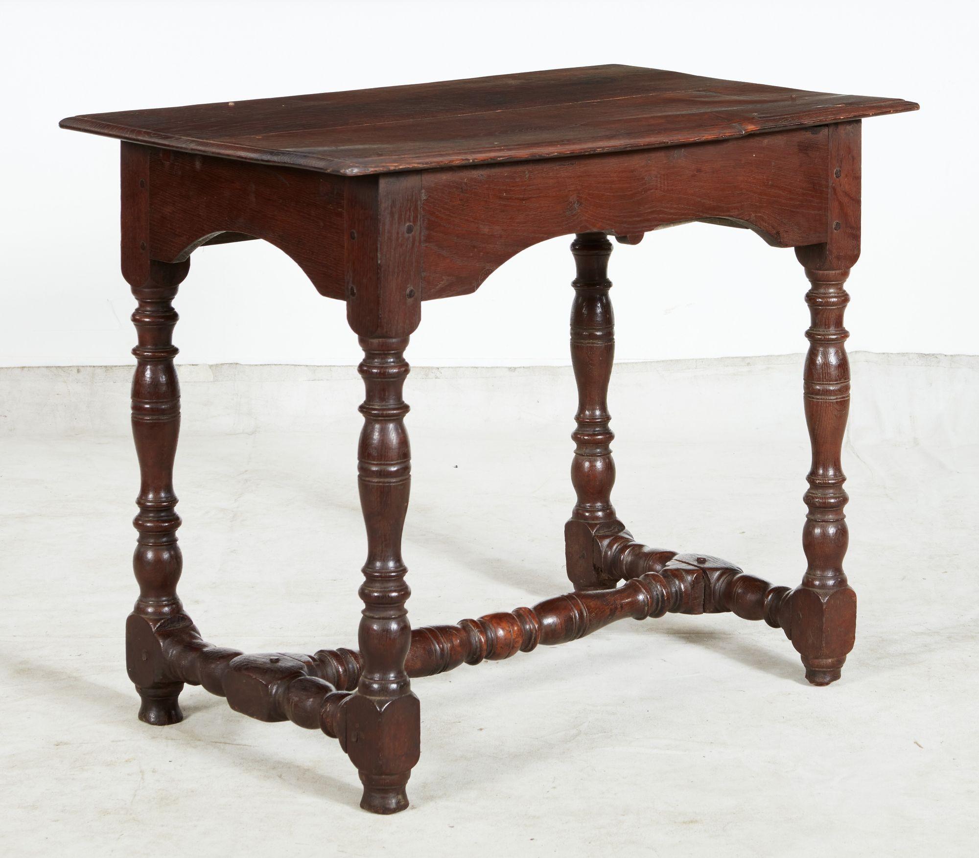 A English table from the reign of James II in oak having joined two-plank top with overhanging molded edge on straight front apron with single drawer having central knob pull, and shaped side and back aprons, on substantial baluster turned legs