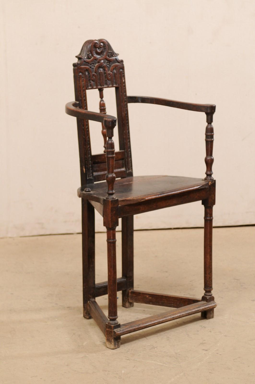 A Spanish carved-wood corner style armchair from the 17th century. This antique chair from Spain features a rectangular-shaped open back with turned post rest set vertically at center, and a beautifully carved top rail in winged scroll motif. The