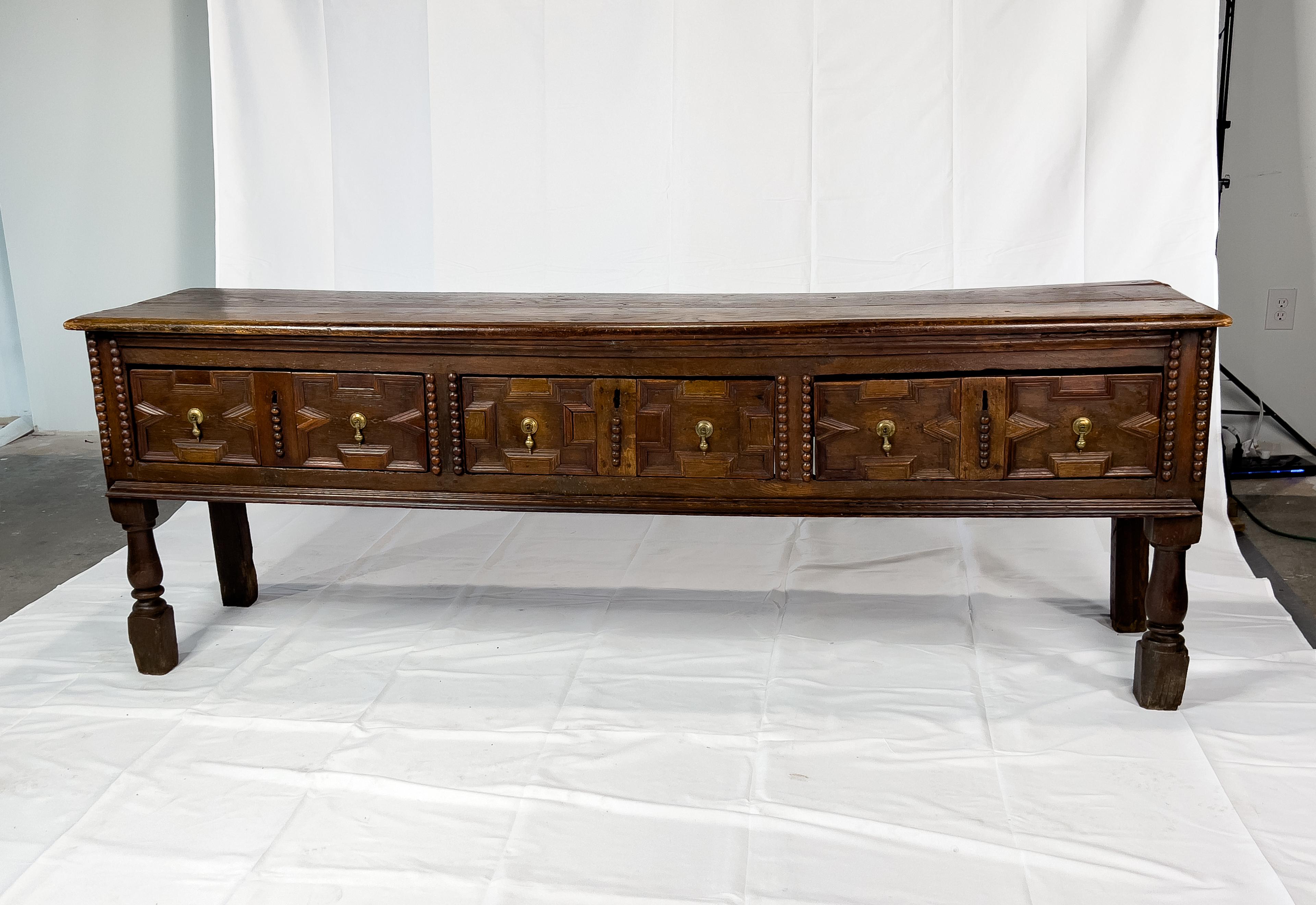 17th c. Oak Spanish console with amazing patina and brass tear drop hardware. The console has three paneled drawers above two turned front legs and two straight back legs.