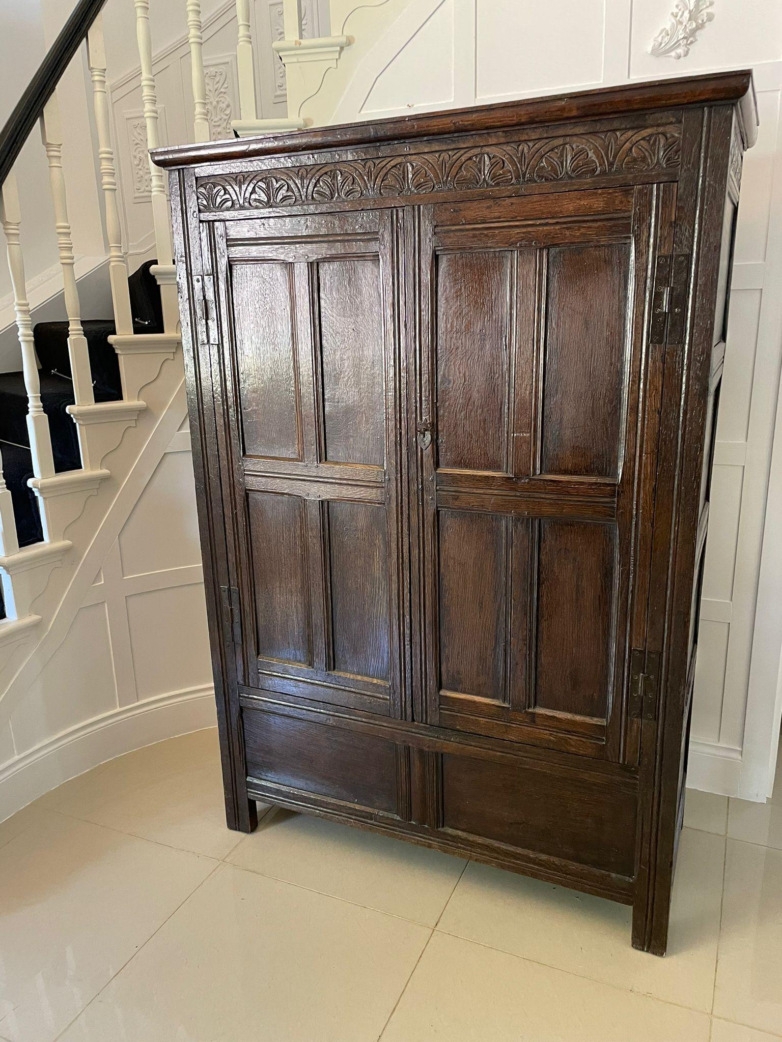 An original 17th century oak hall cupboard with a moulded cornice and a quality carved frieze above a pair of oak moulded panelled doors with original wrought iron hinges opening to reveal a hanging or storage compartment, moulded panelled sides