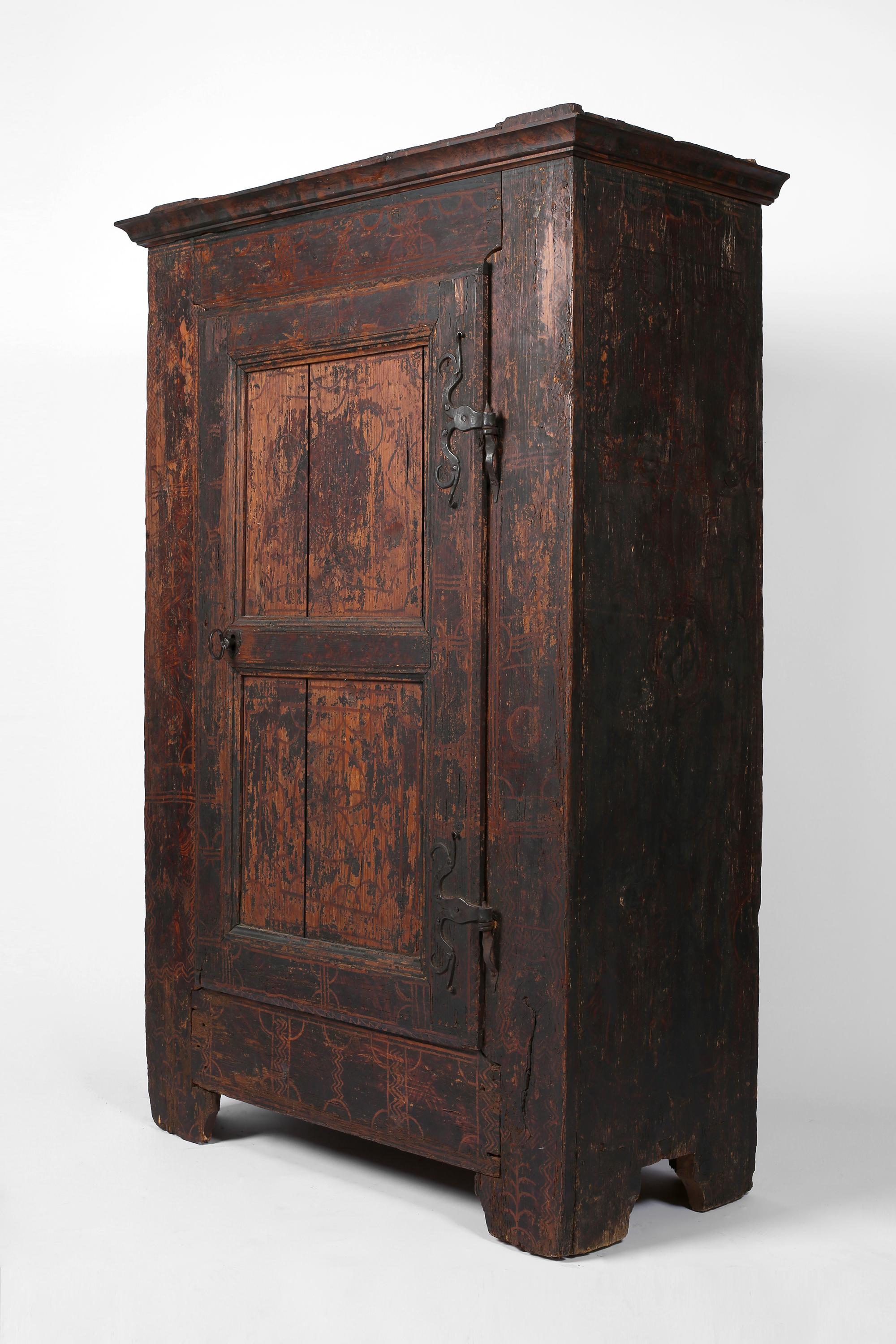 A striking, late 17th century heavily patinated pine cupboard from the alpine region of Styria. Featuring intricately forged iron hardware and remnants of historic folk paintwork, with original working lock and key. The panelled door opens to reveal