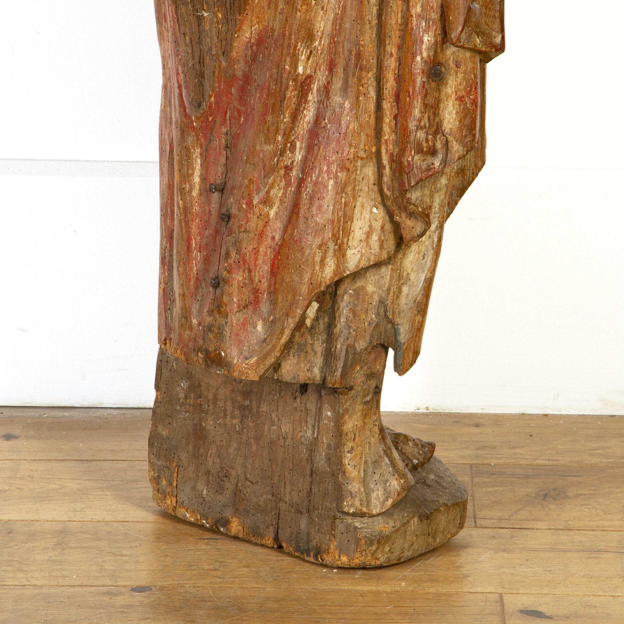 Mid 17th century Northern European carved figure of a saint. 
This striking statue depicts a saint who is dressed in robes, whilst holding his hand over his heart. This figure is freestanding and is stood within a leaning position which makes him