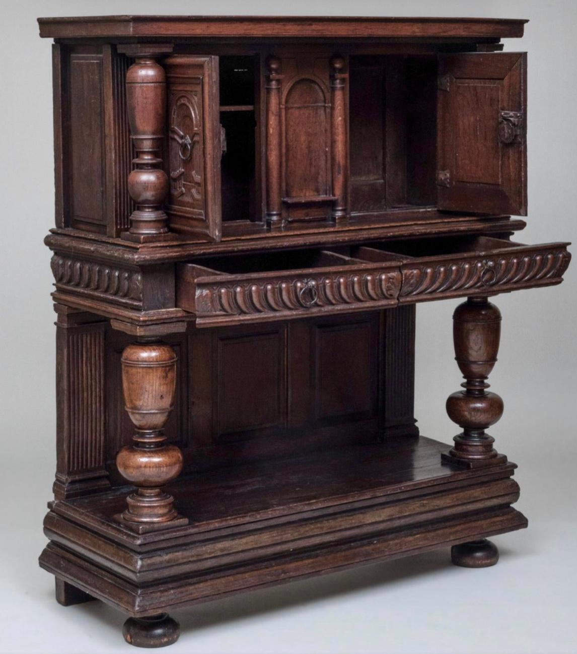 This is a fabulous quality, heavily carved solid oak court cupboard, made in England. The geometric moldings on the panels and doors are wonderfully carved. The quality and depth of all the hand carving is amazing. The turned columns add character.