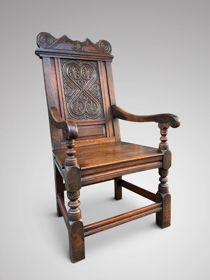 A superb and original carved oak Wainscot armchair, likely Yorkshire, United Kingdom, with a large lozenge carved panel to the back and carved crest rail and ears of scrolling. Raised on turned gun barrel legs with block feet, each joined by moulded