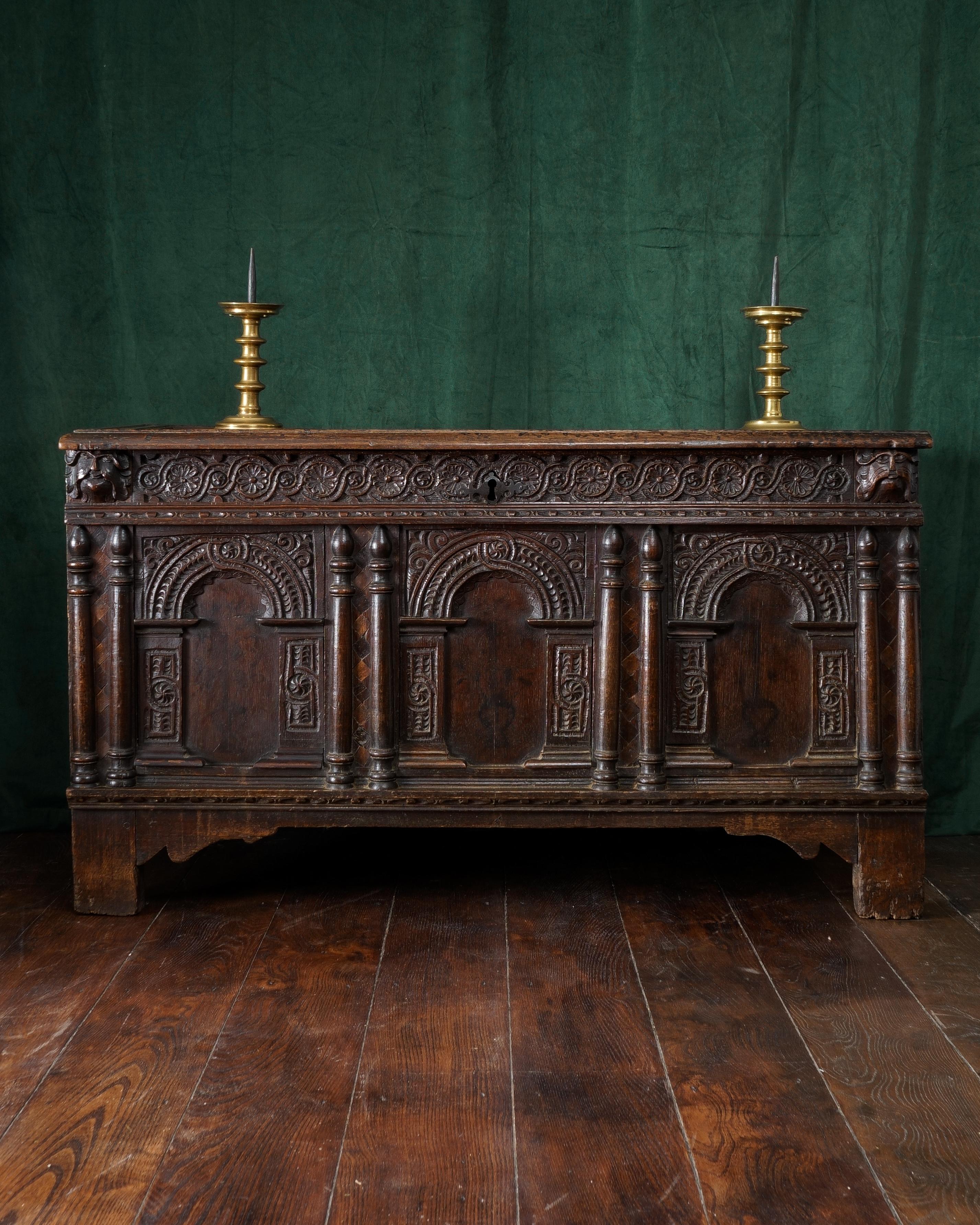 The triple panelled lid with broad and flat run-moulded rails, the front with three panels, each with stained-black foliage issuing from baluster shaped vases, enclosed within a finely gauge and cable-carved arcade, spaced by applied split